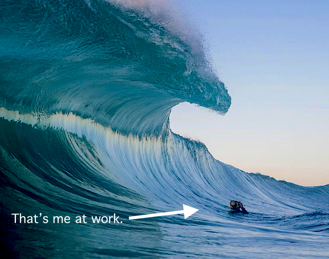 Person surfing a large wave with text 'That's me at work.'