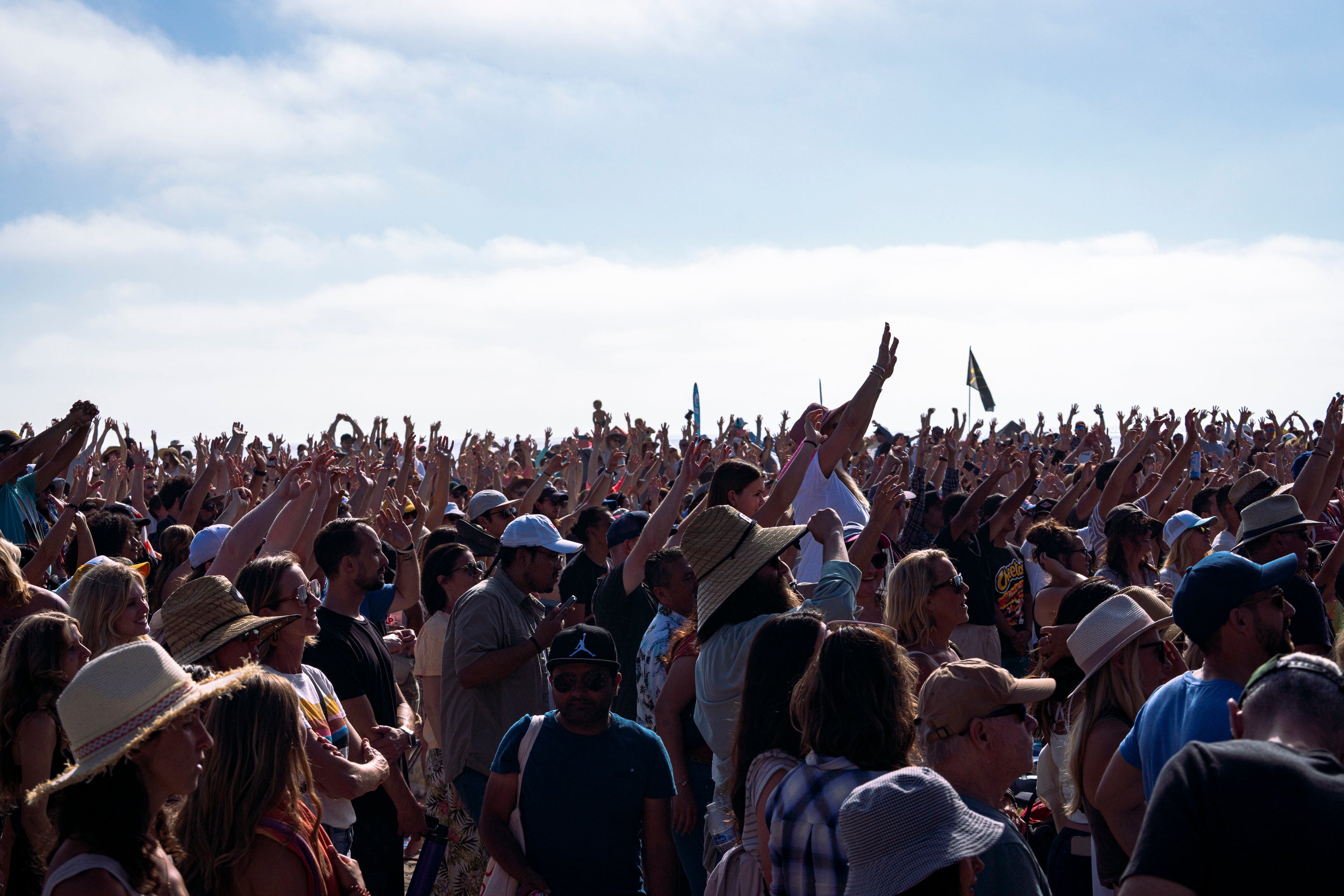 Large crowd of people with raised hands against a blue sky.