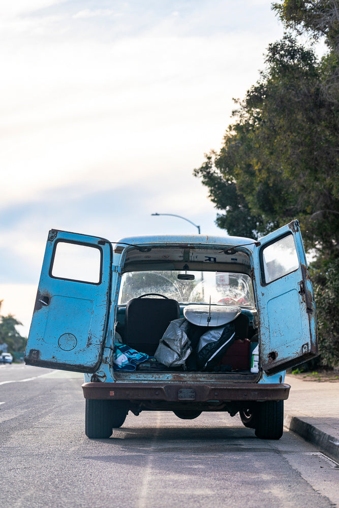 Back of a blue van with open doors on a road with trees in the background