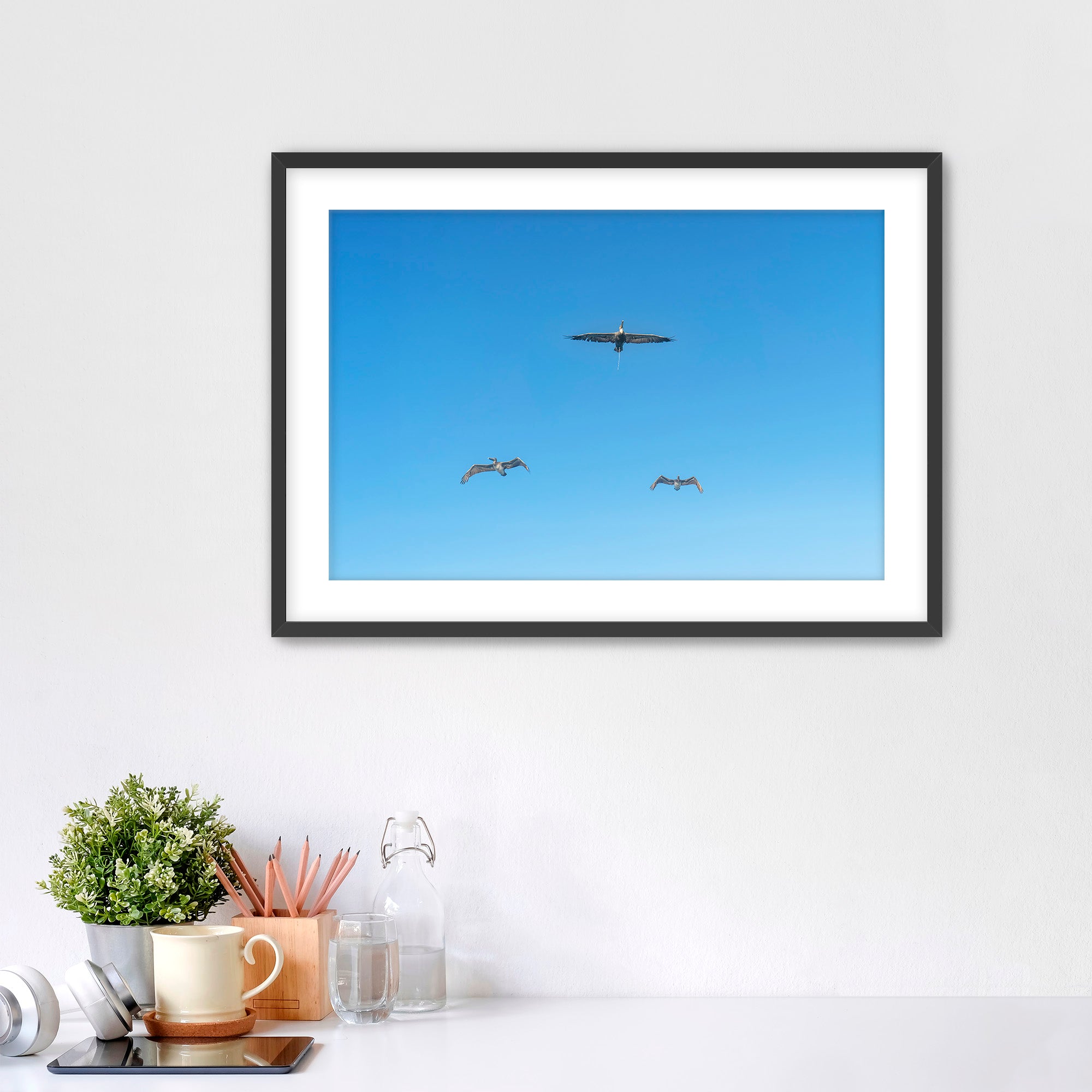 Framed artwork of birds flying in a blue sky on a white wall.