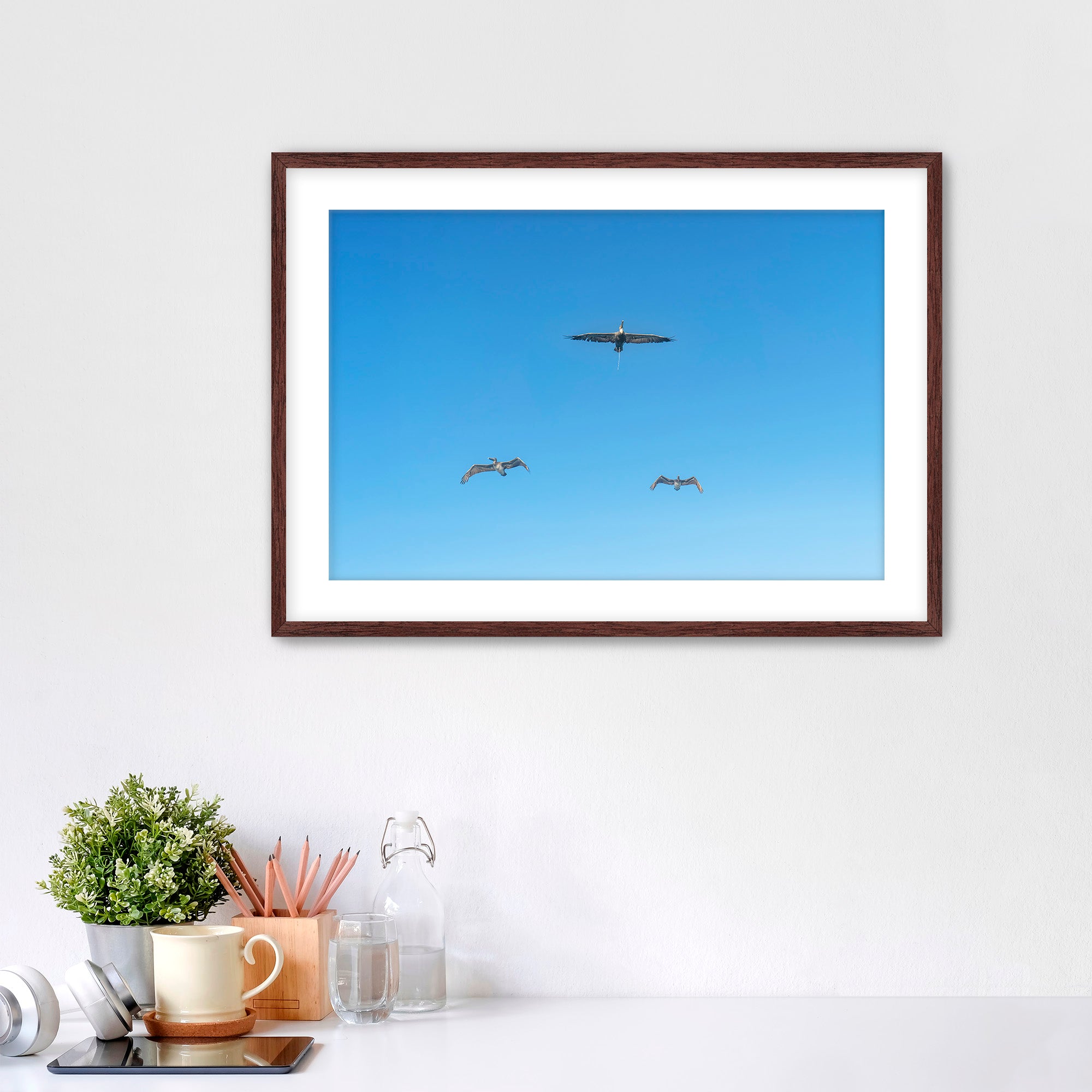 Framed artwork of birds flying in a blue sky on a white wall.