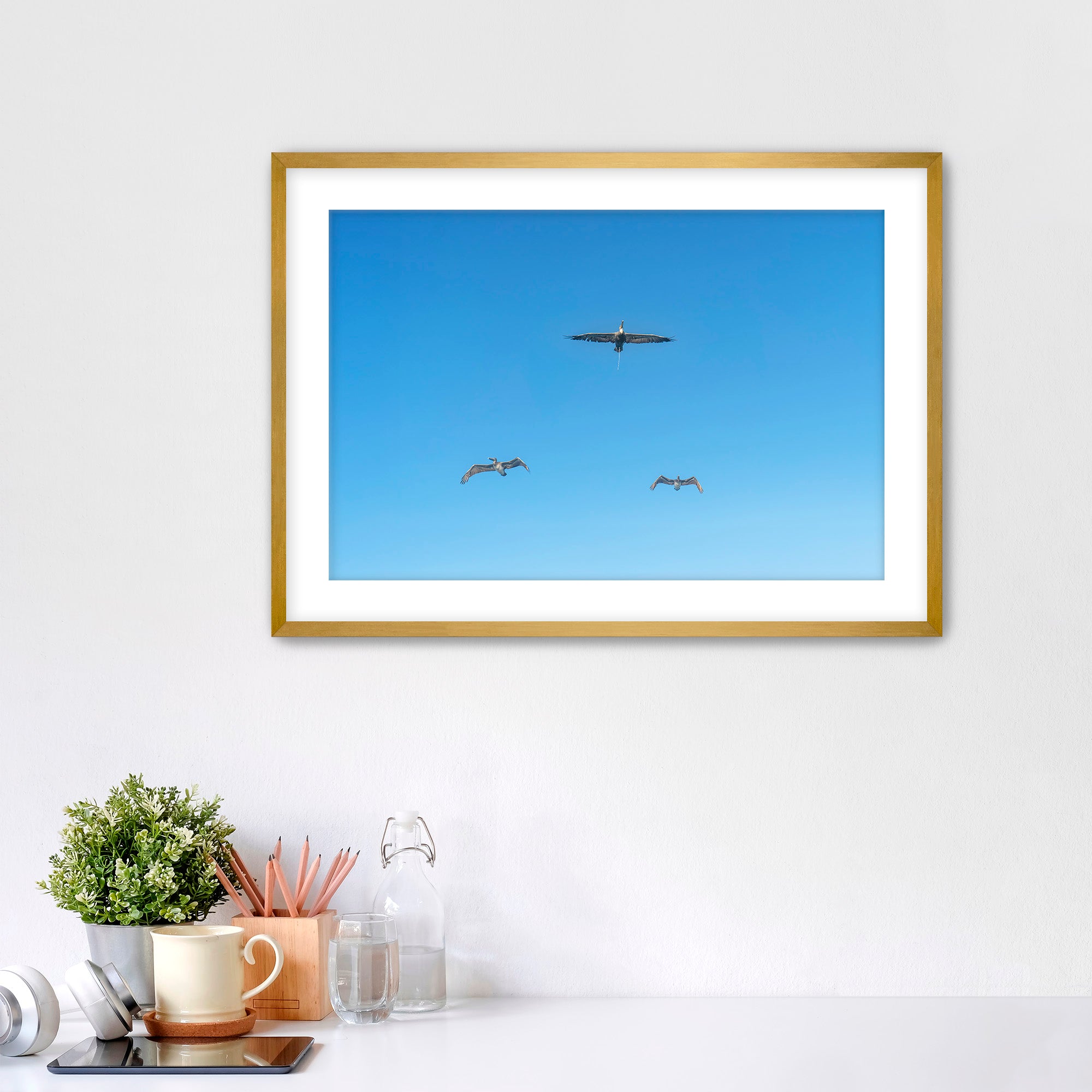 Framed artwork of birds flying in a blue sky on a white wall.