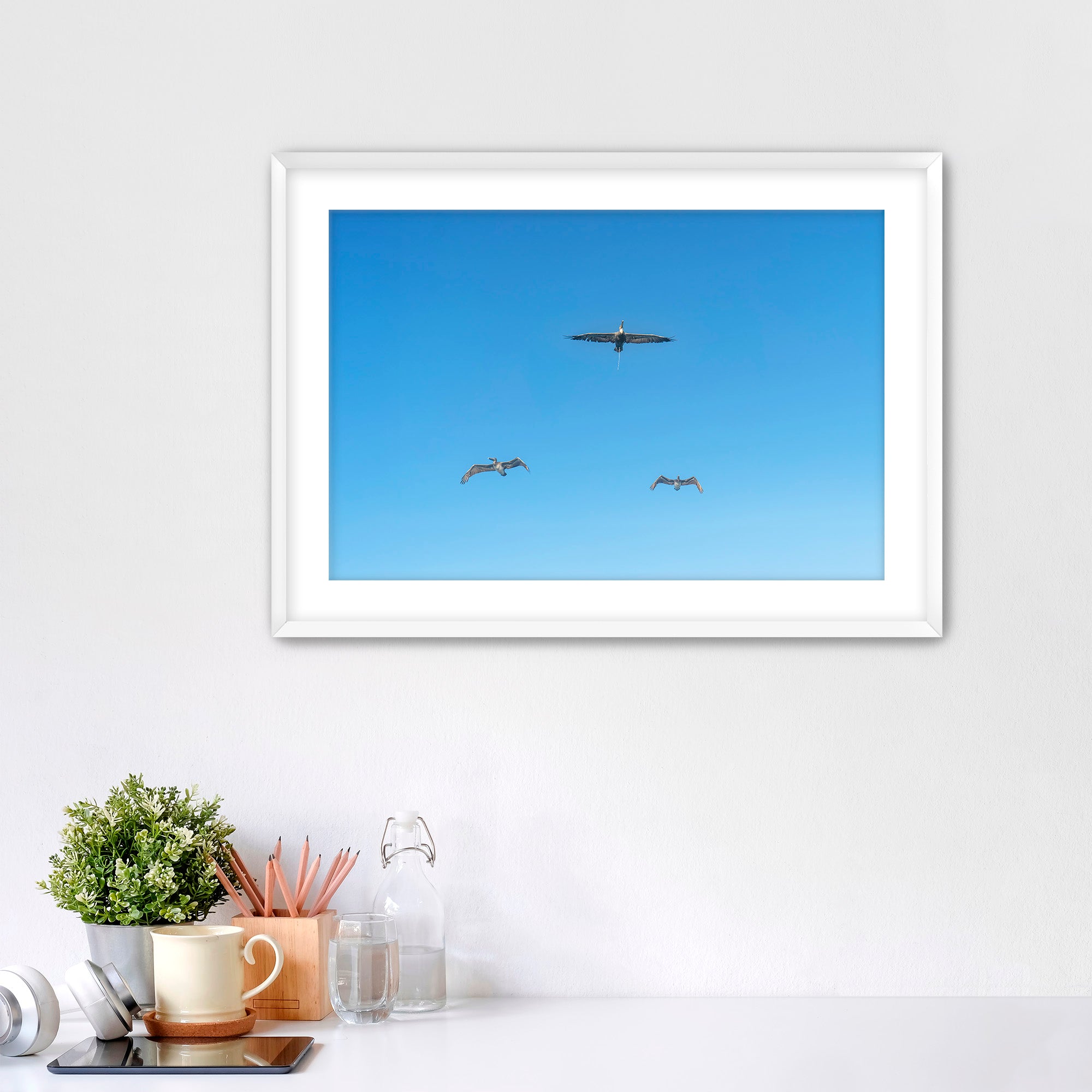 Framed artwork of birds flying in a blue sky on a white wall.