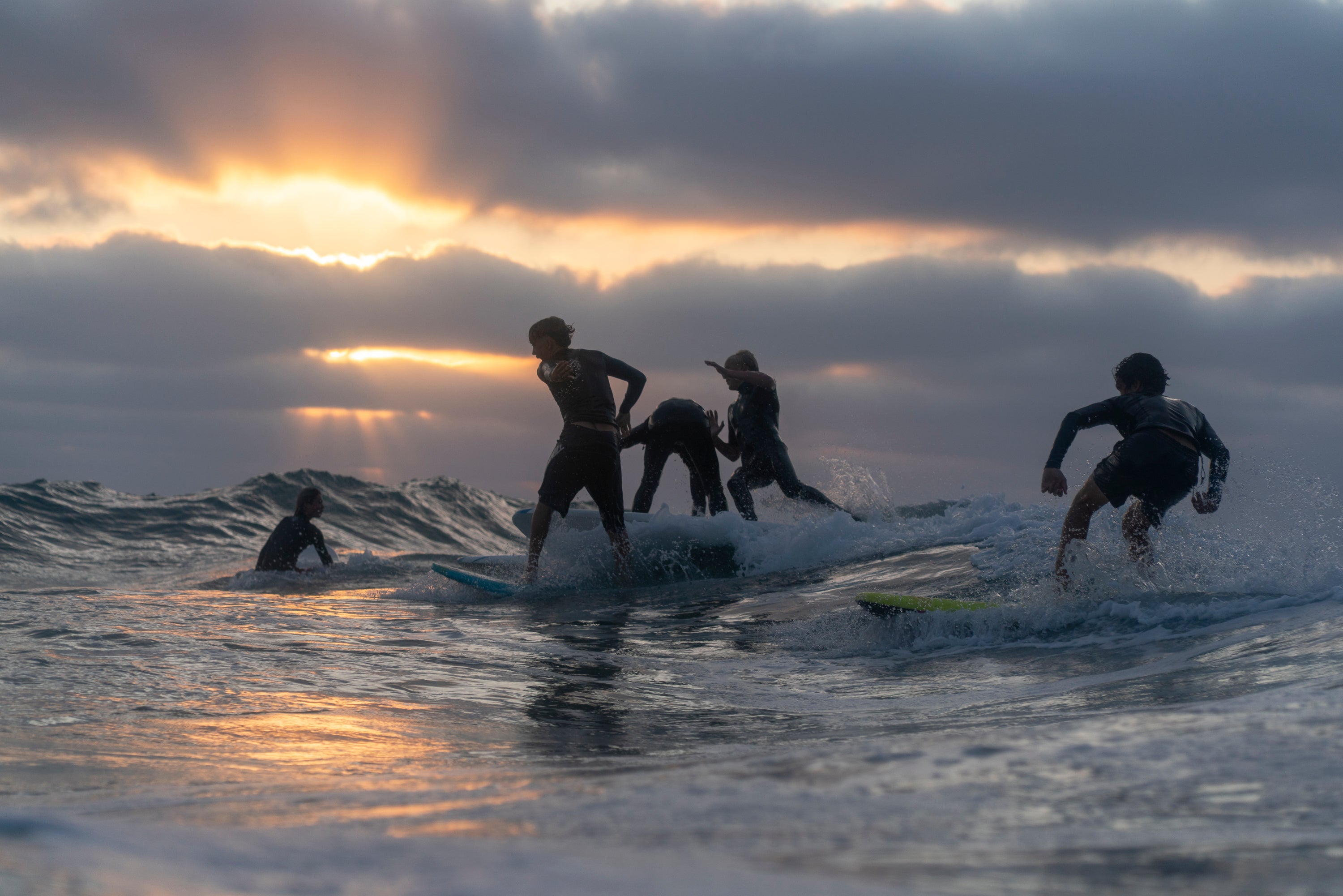 Surfers in wetsuits on a wave during sunset.