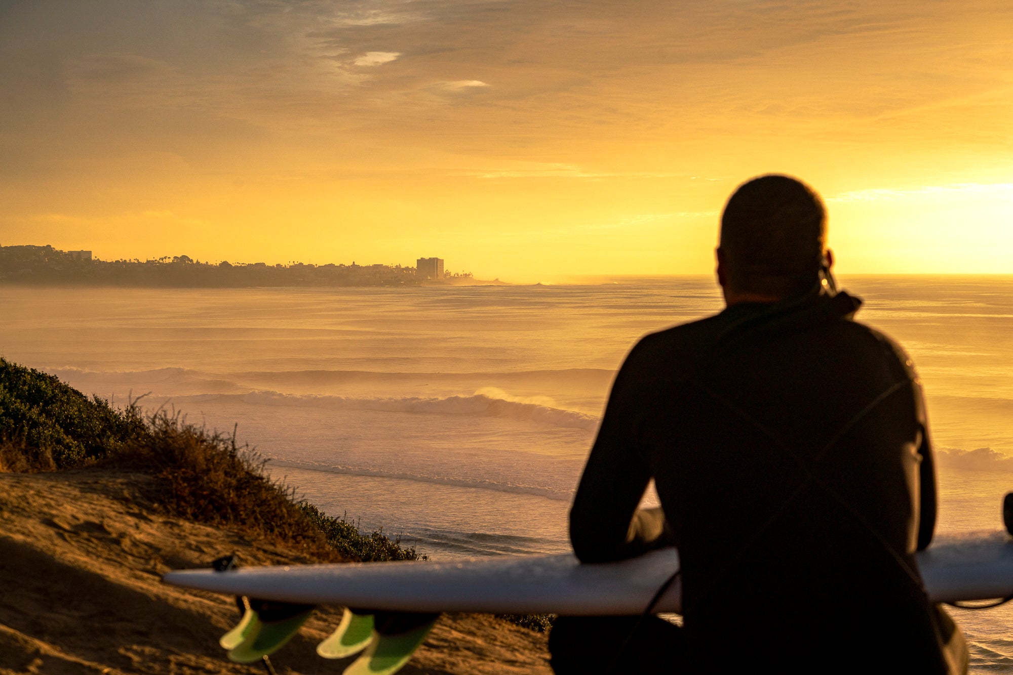 Surfer sitting on the cliff overlooking Black's Beach in La Jolla California at sunset. 