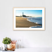 Beach scene with corduroy sand, ocean waves and a distant power plant on a white wall with desk items below. 