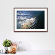 Framed artwork of a wave breaking with the Carlsbad smoke stack on a white wall above a desk with office supplies.