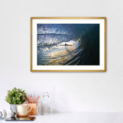 Framed artwork of a wave breaking with the Carlsbad smoke stack on a white wall above a desk with office supplies.