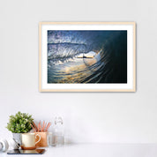 Framed artwork of a wave breaking with the Carlsbad smoke stack on a white wall above a desk with office supplies.
