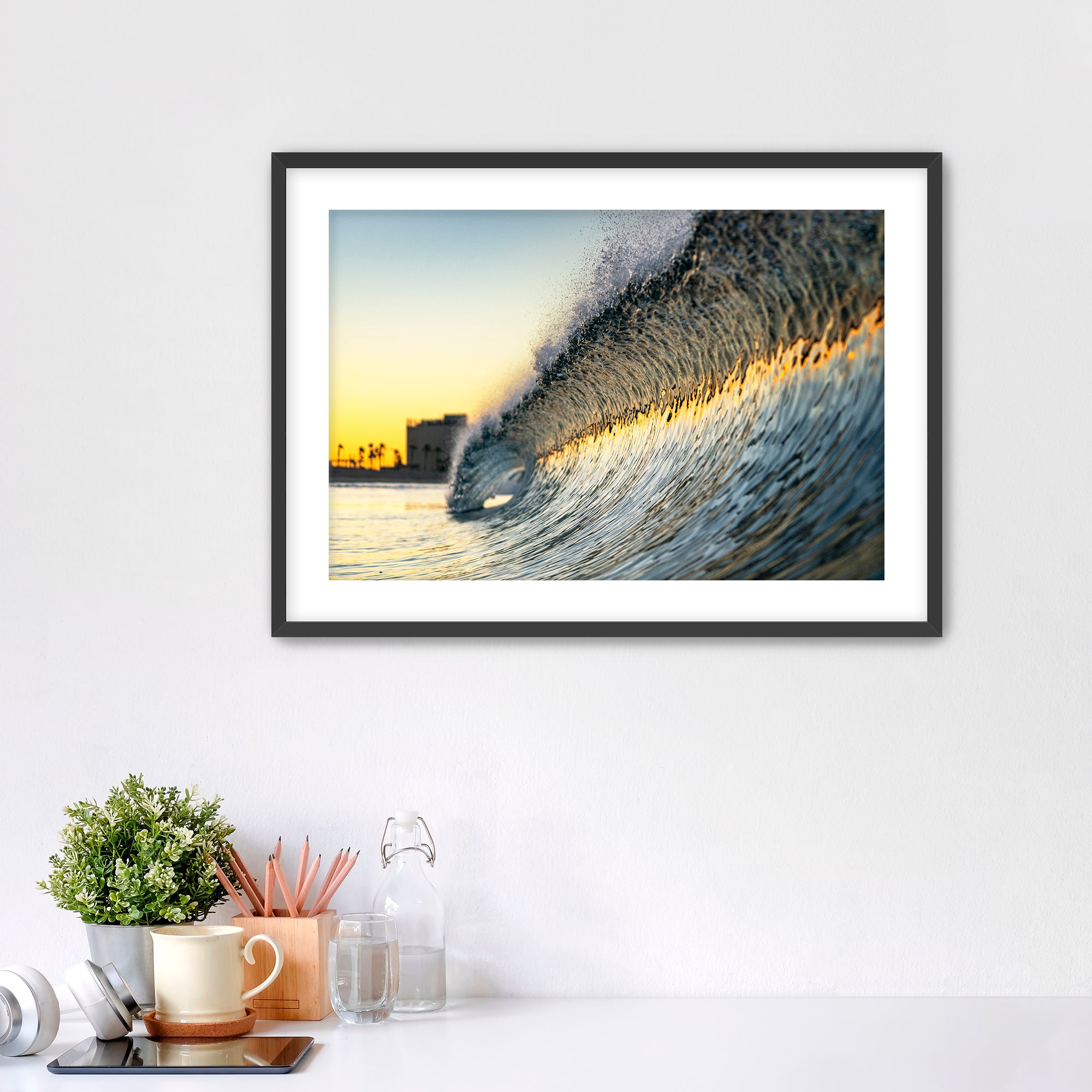 Framed photograph of a colorful wave crashing on South Carlsbad State beach with office items below. 