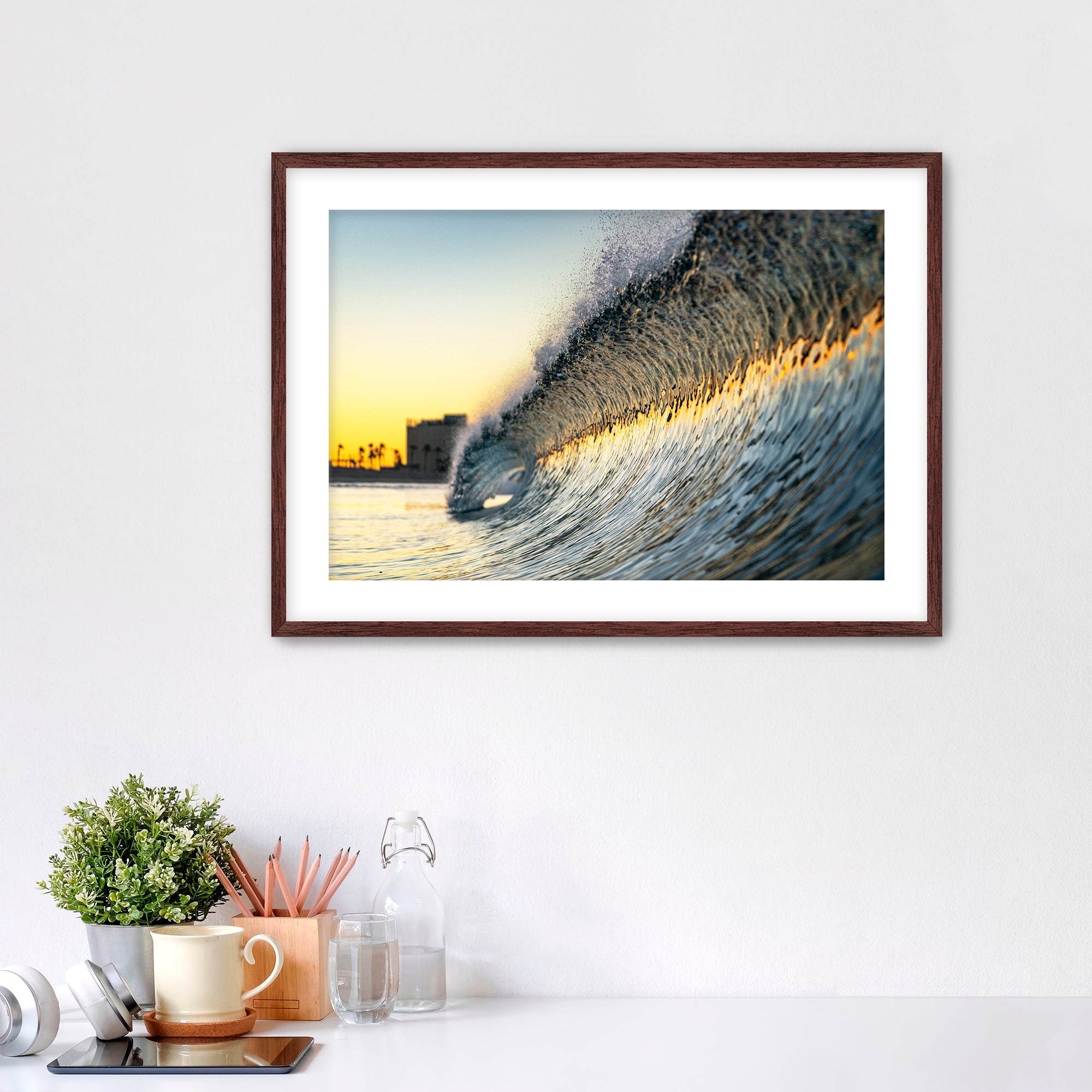 Framed photograph of a colorful wave crashing on South Carlsbad State beach with office items below. 