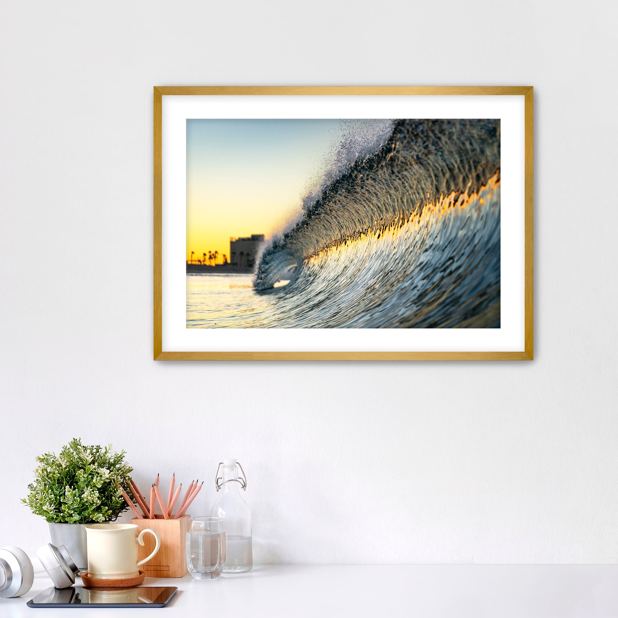 Framed photograph of a colorful wave crashing on South Carlsbad State beach with office items below. 