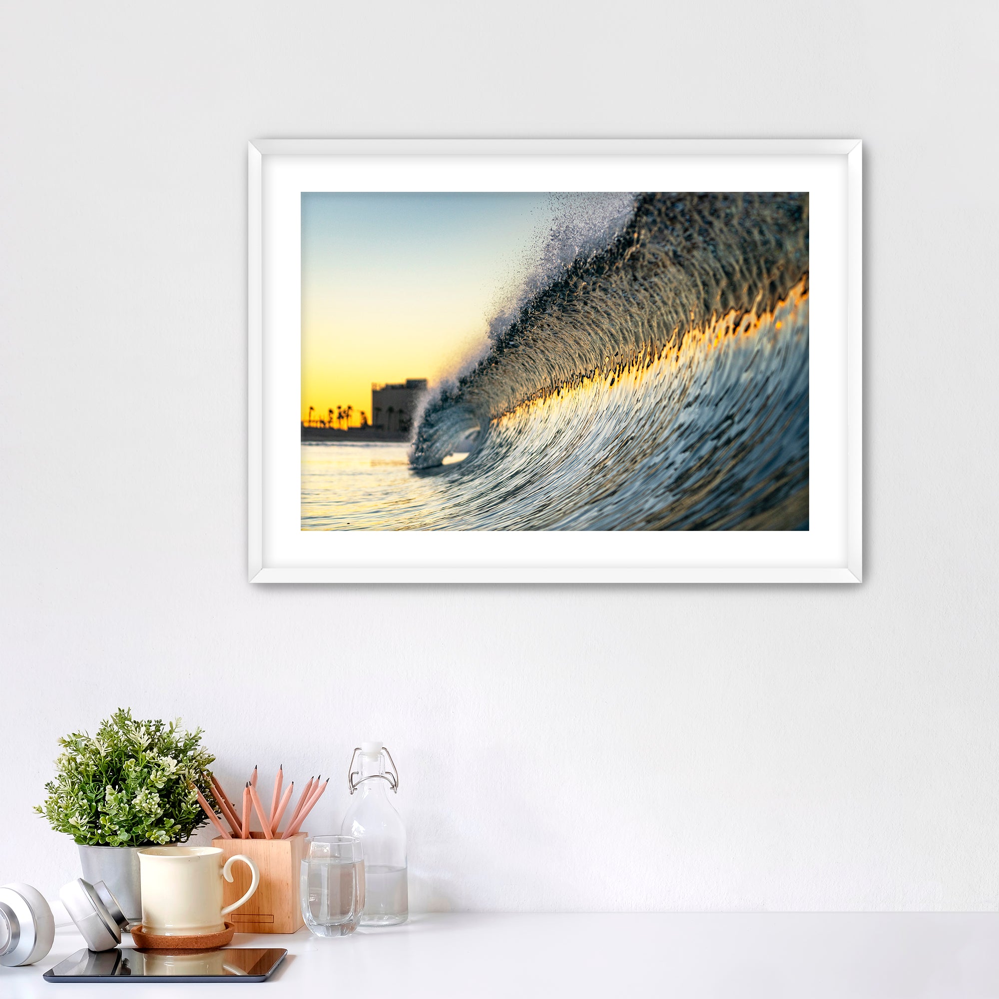 Framed photograph of a colorful wave crashing on South Carlsbad State beach with office items below. 