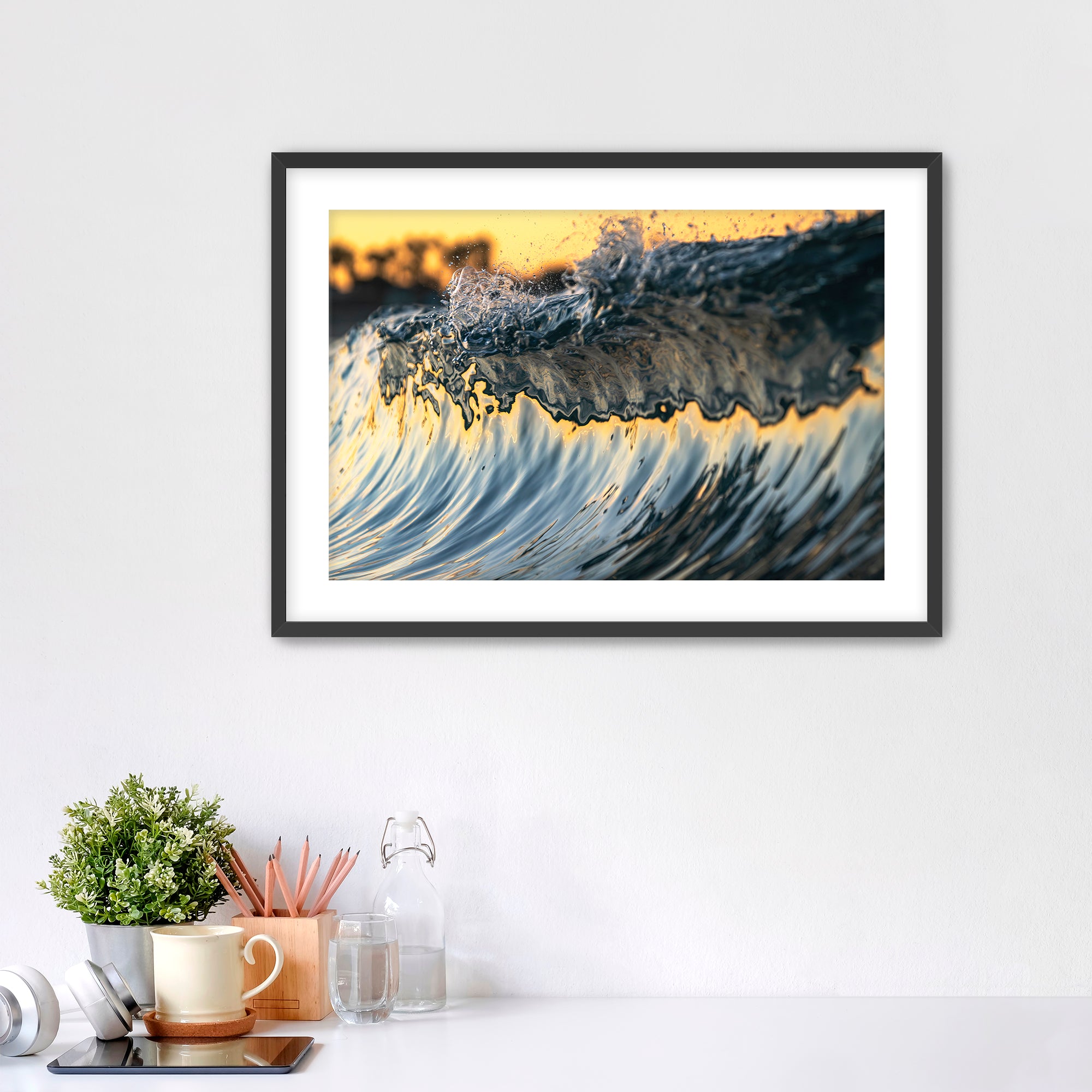 Framed abstract art piece of wave details on a white wall with desk items below. 