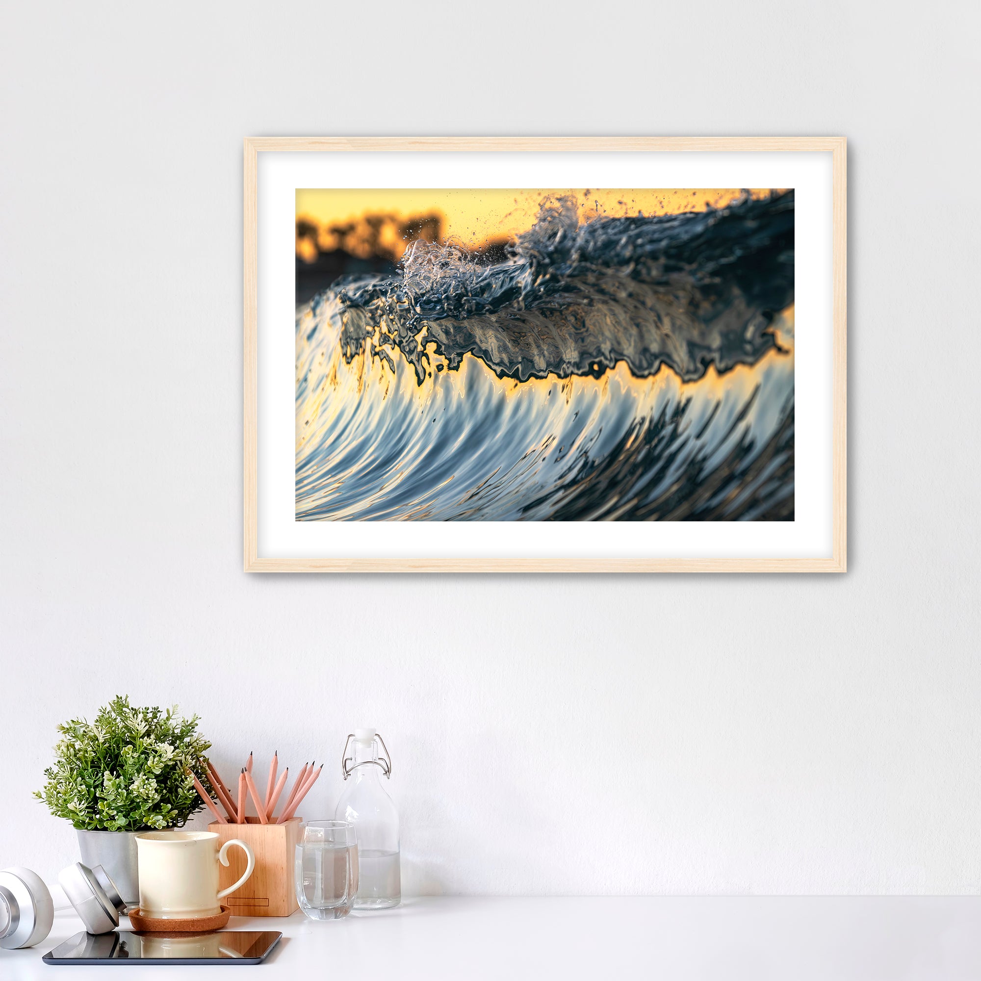 Framed abstract art piece of wave details on a white wall with desk items below. 
