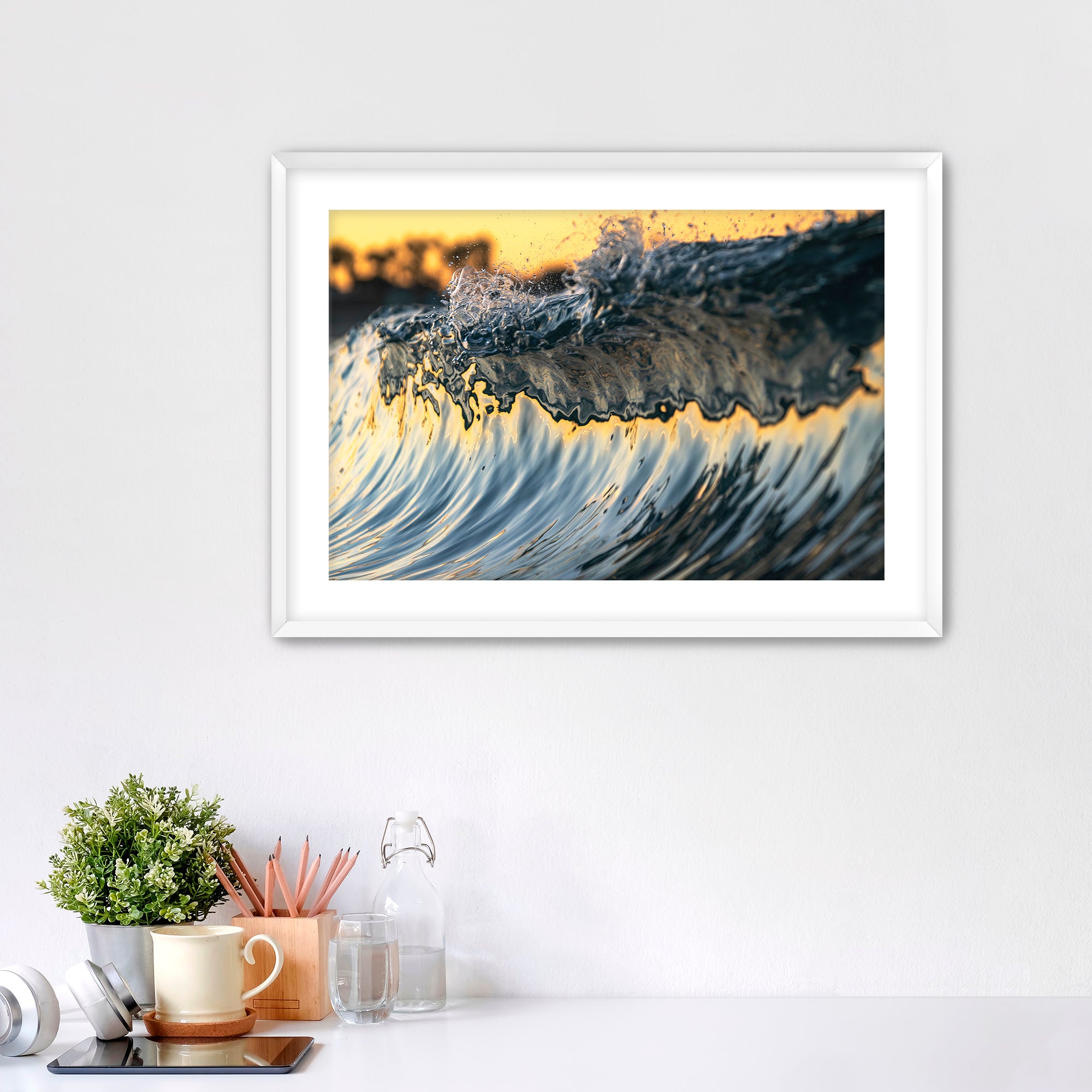 Framed abstract art piece of wave details on a white wall with desk items below. 