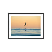 Framed artwork of a pelican flying over water at sunrise.