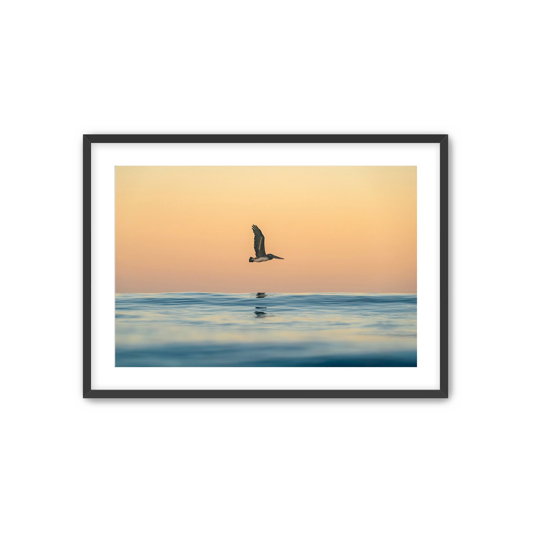 Framed artwork of a pelican flying over water at sunrise.