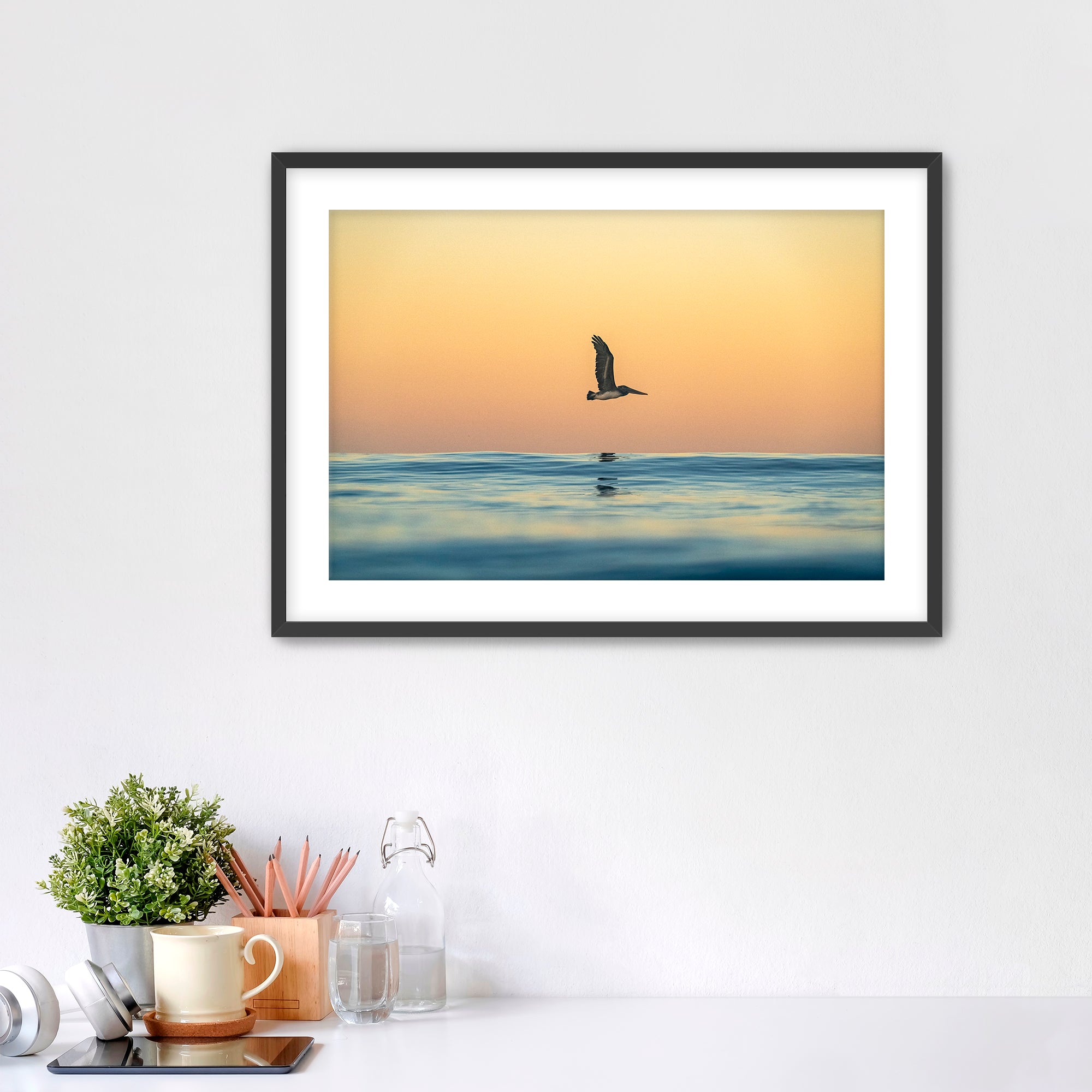 Framed photograph of a pelican over water in sunrise light. 