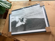 Vintage-style black and white photo of a surfer on a wave, framed and placed on cardboard.