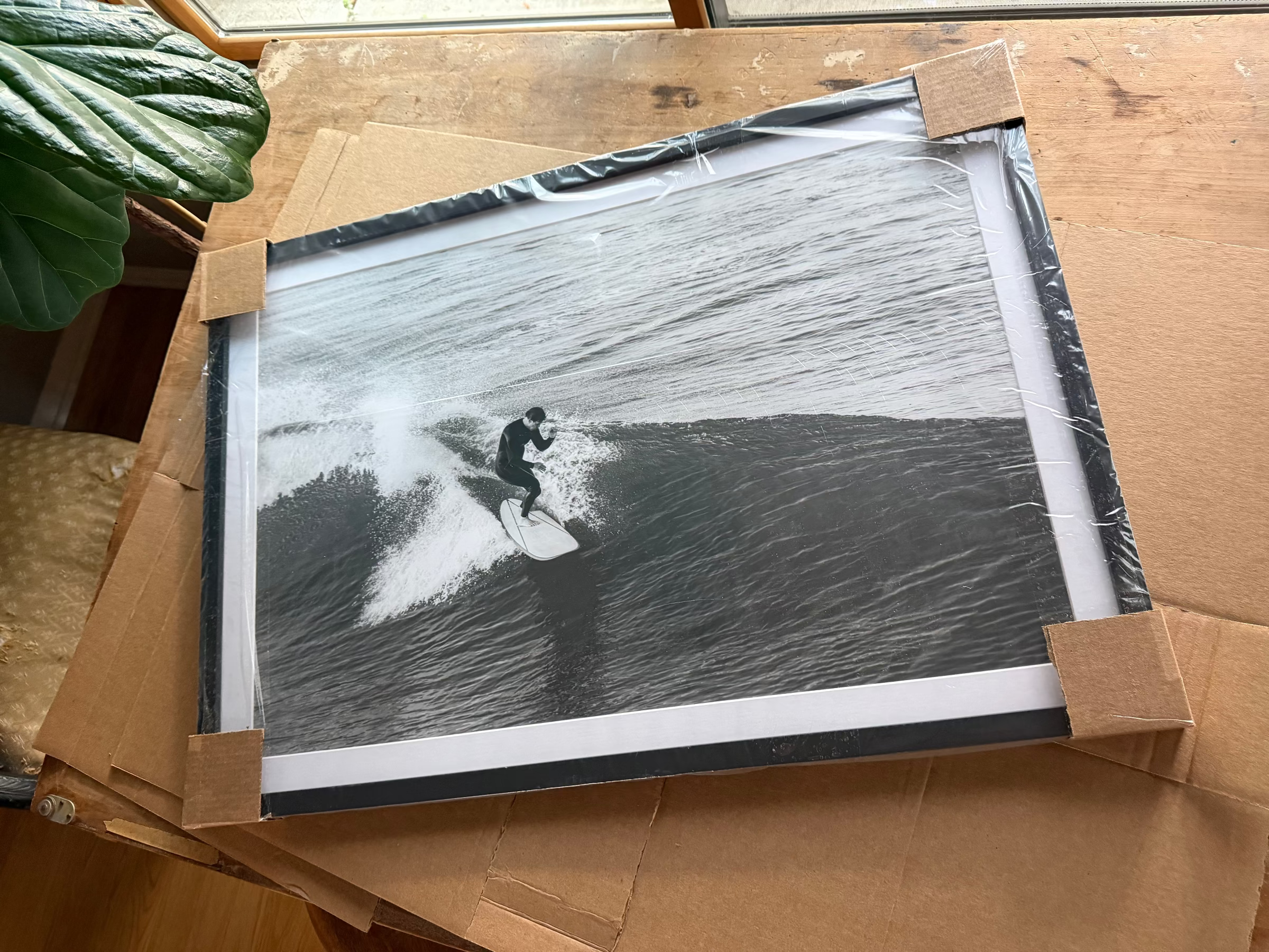 Vintage-style black and white photo of a surfer on a wave, framed and placed on cardboard.