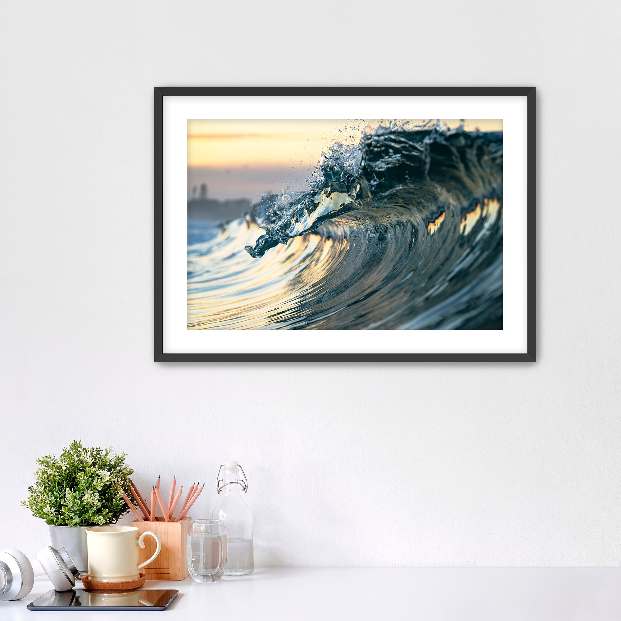 Framed photograph of a wave like a jewel on a wall above a desk with office supplies.