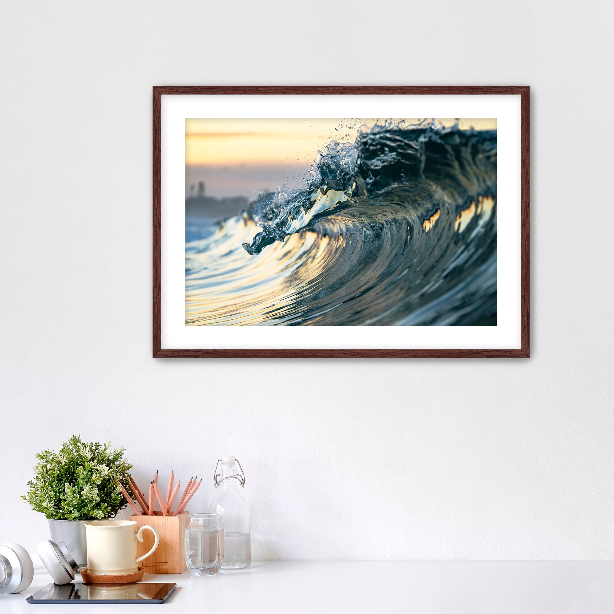 Framed photograph of a wave like a jewel on a wall above a desk with office supplies.