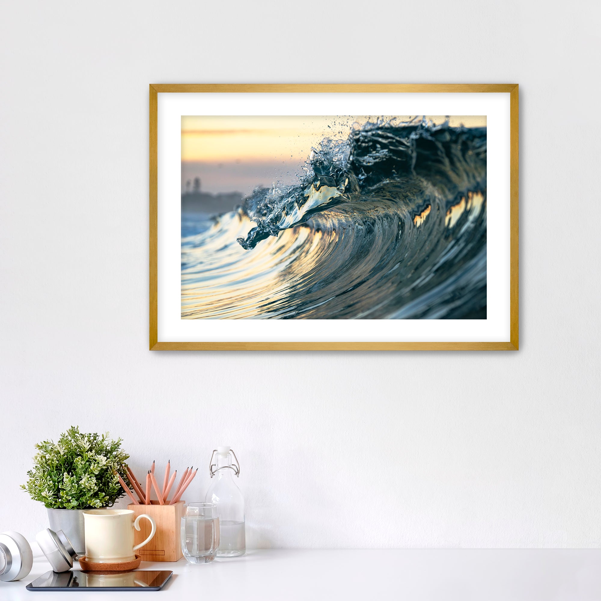 Framed photograph of a wave like a jewel on a wall above a desk with office supplies.