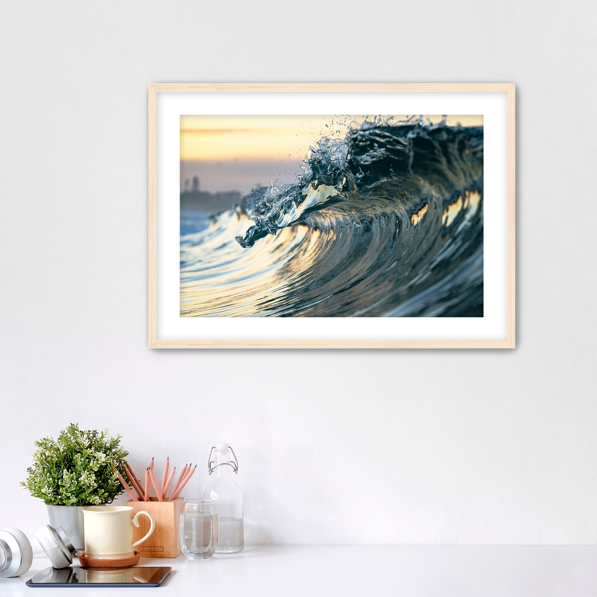 Framed photograph of a wave like a jewel on a wall above a desk with office supplies.