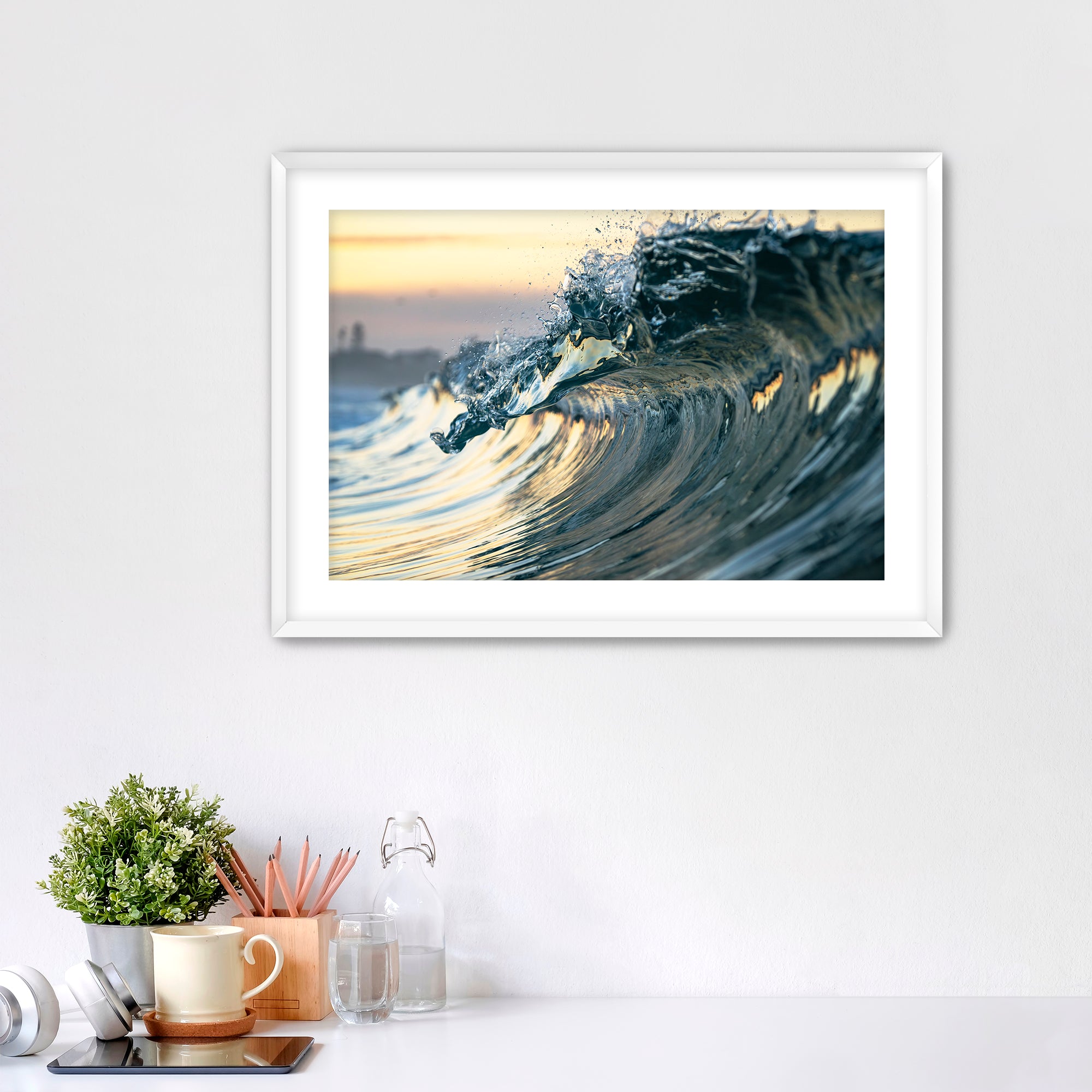 Framed photograph of a wave like a jewel on a wall above a desk with office supplies.