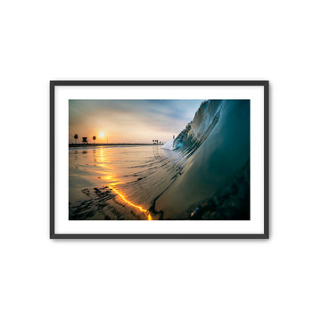 Framed photograph of a sunrise at the beach with a wave crashing.