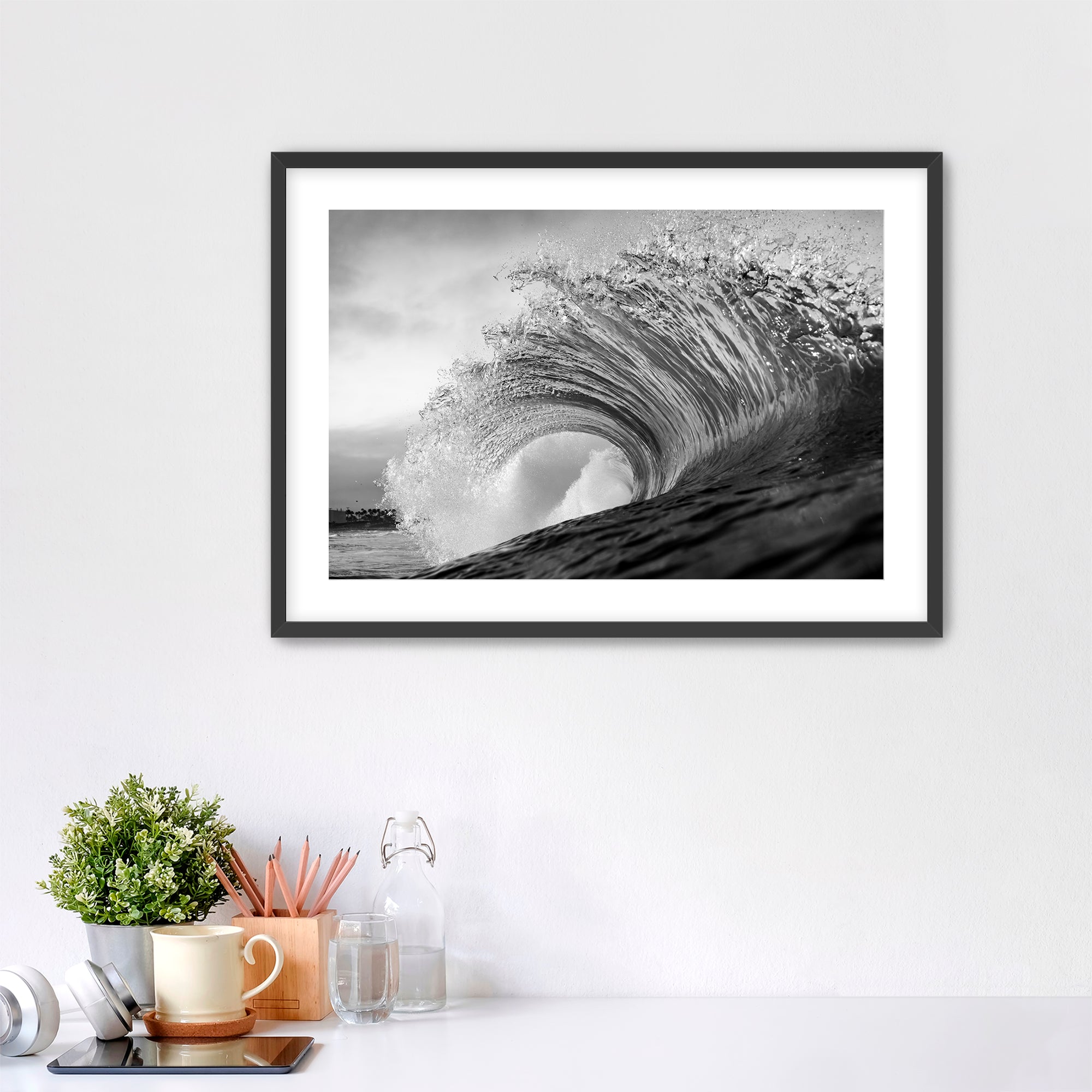 Framed black and white wave art print shot next to the Pacific Coast Highway at South Carlsbad State Beach in Carlsbad, California on a wall above a desk with office supplies.