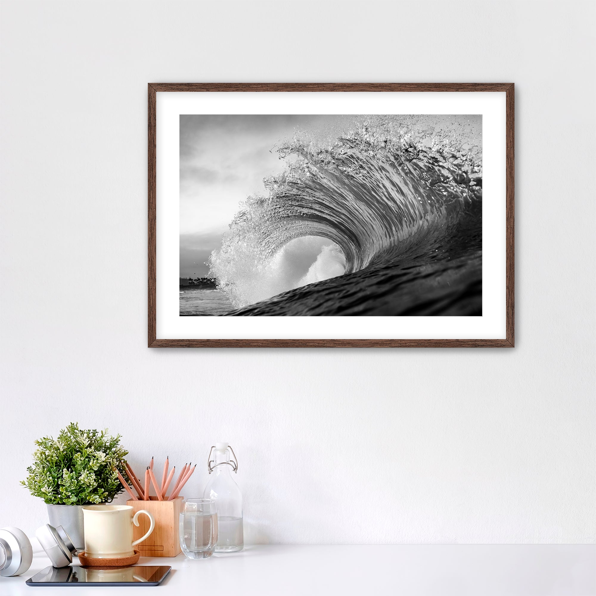 Framed black and white wave art print shot next to the Pacific Coast Highway at South Carlsbad State Beach in Carlsbad, California on a wall above a desk with office supplies.