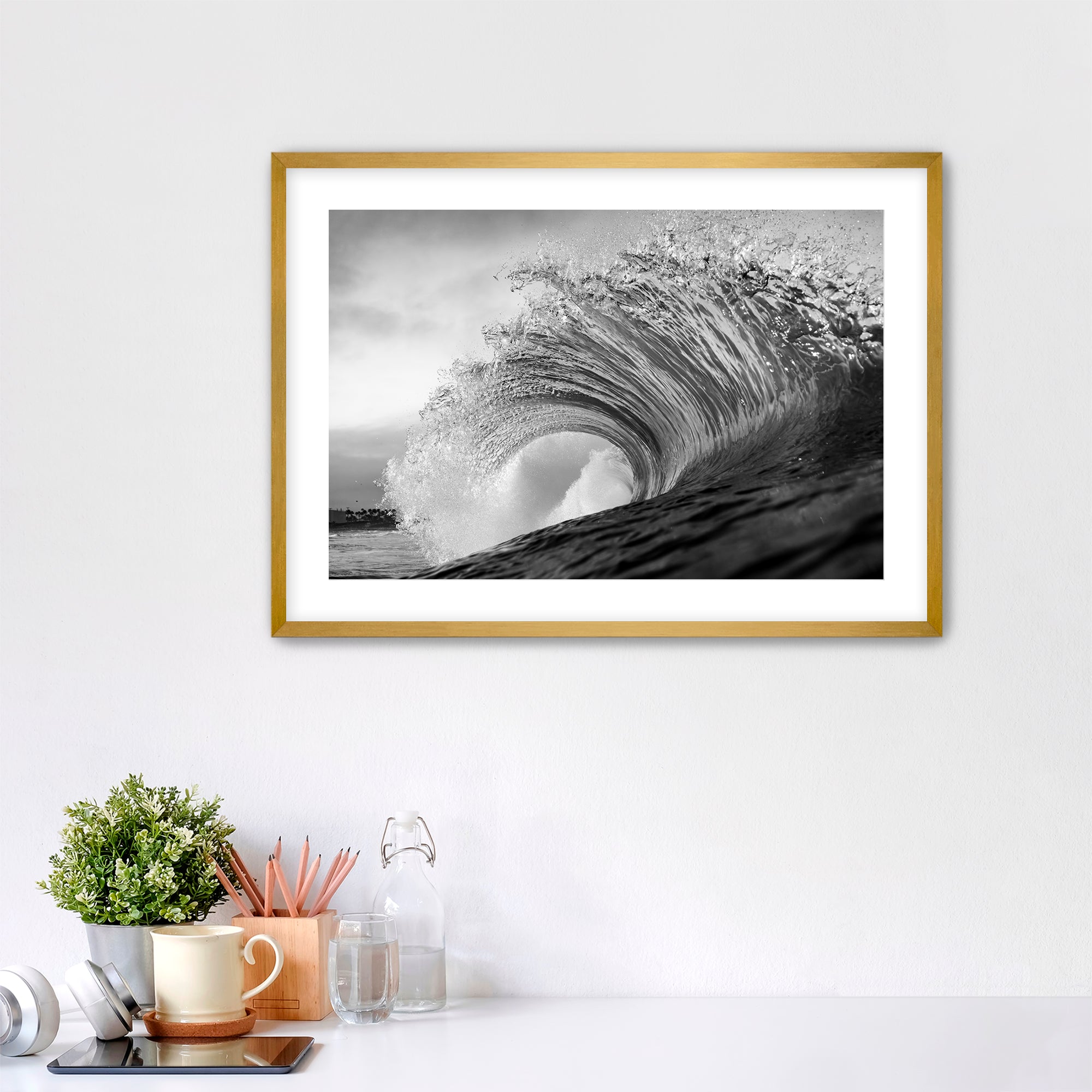 Framed black and white wave art print shot next to the Pacific Coast Highway at South Carlsbad State Beach in Carlsbad, California on a wall above a desk with office supplies.