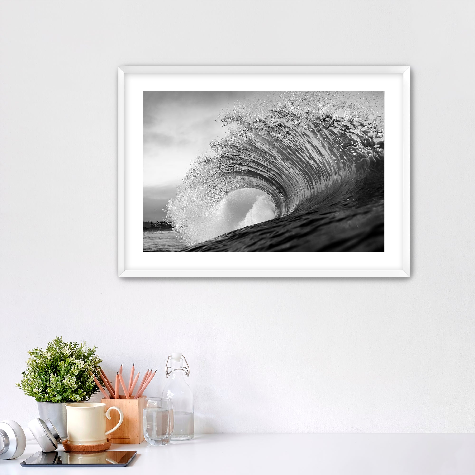 Framed black and white wave art print shot next to the Pacific Coast Highway at South Carlsbad State Beach in Carlsbad, California on a wall above a desk with office supplies.