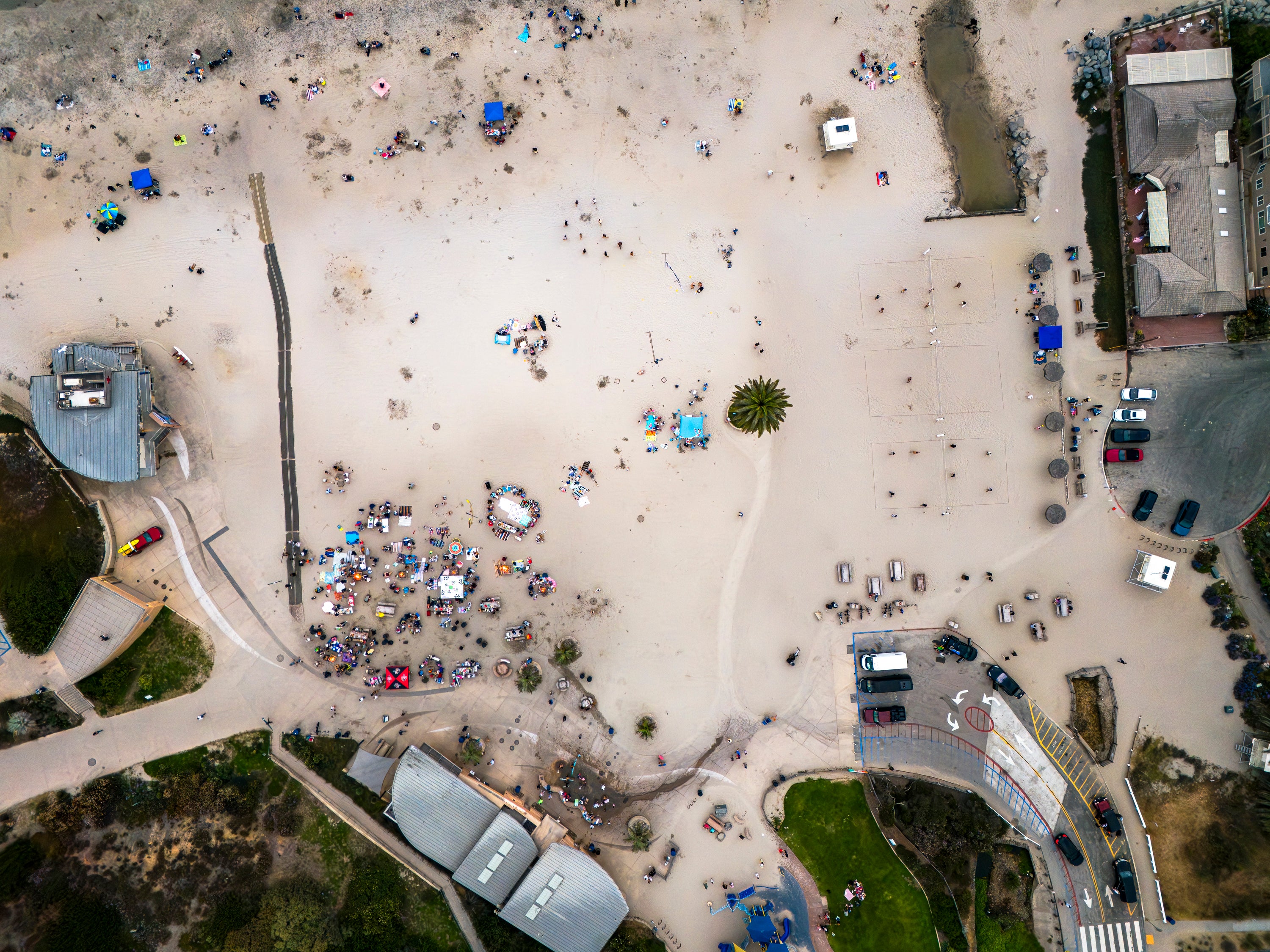 Aerial view of Moonlight Beach in Encinitas with people, cars, campfires, and buildings.
