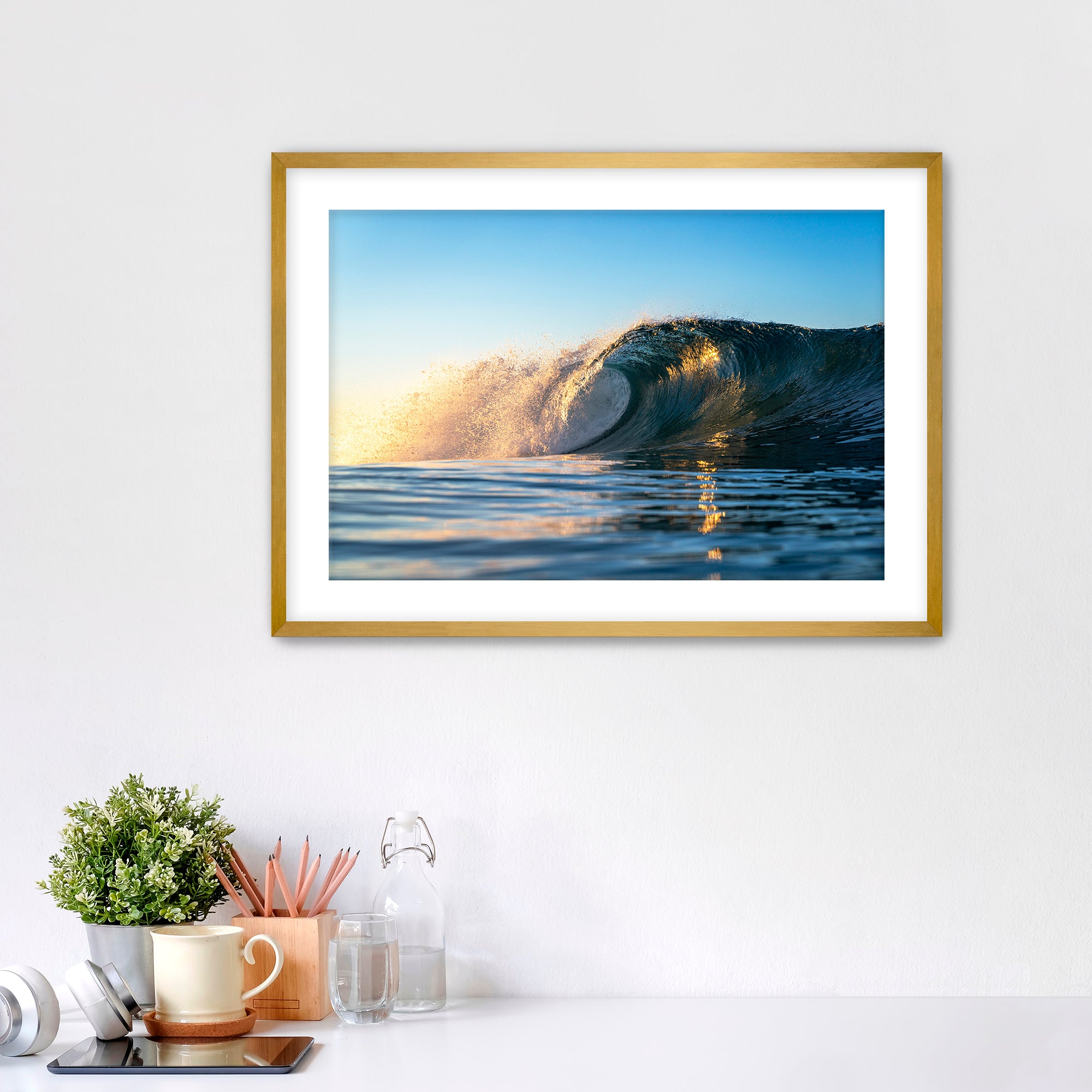 Framed photograph of a crisp morning wave in Carlsbad on a wall above a desk with office supplies.