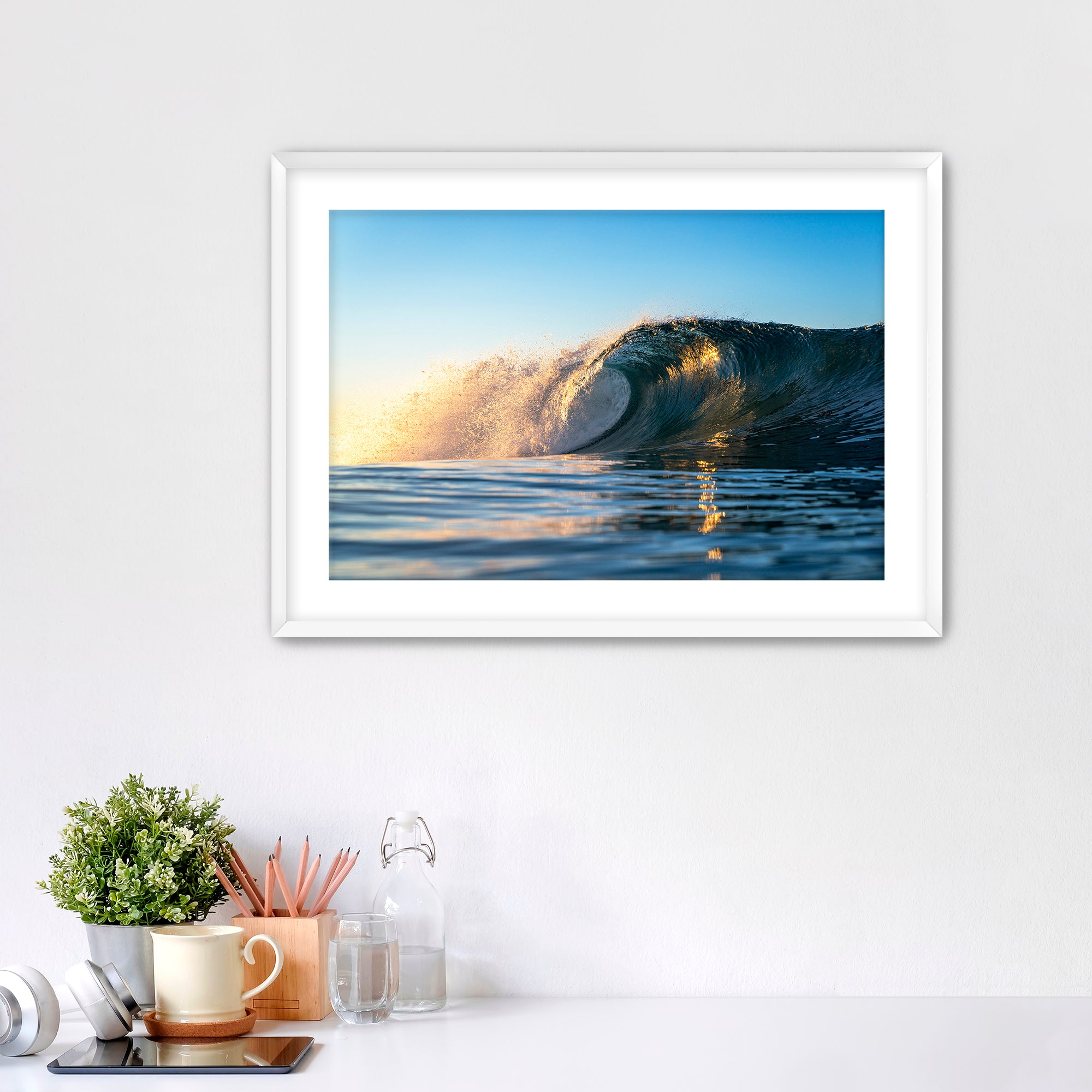 Framed photograph of a crisp morning wave in Carlsbad on a wall above a desk with office supplies.
