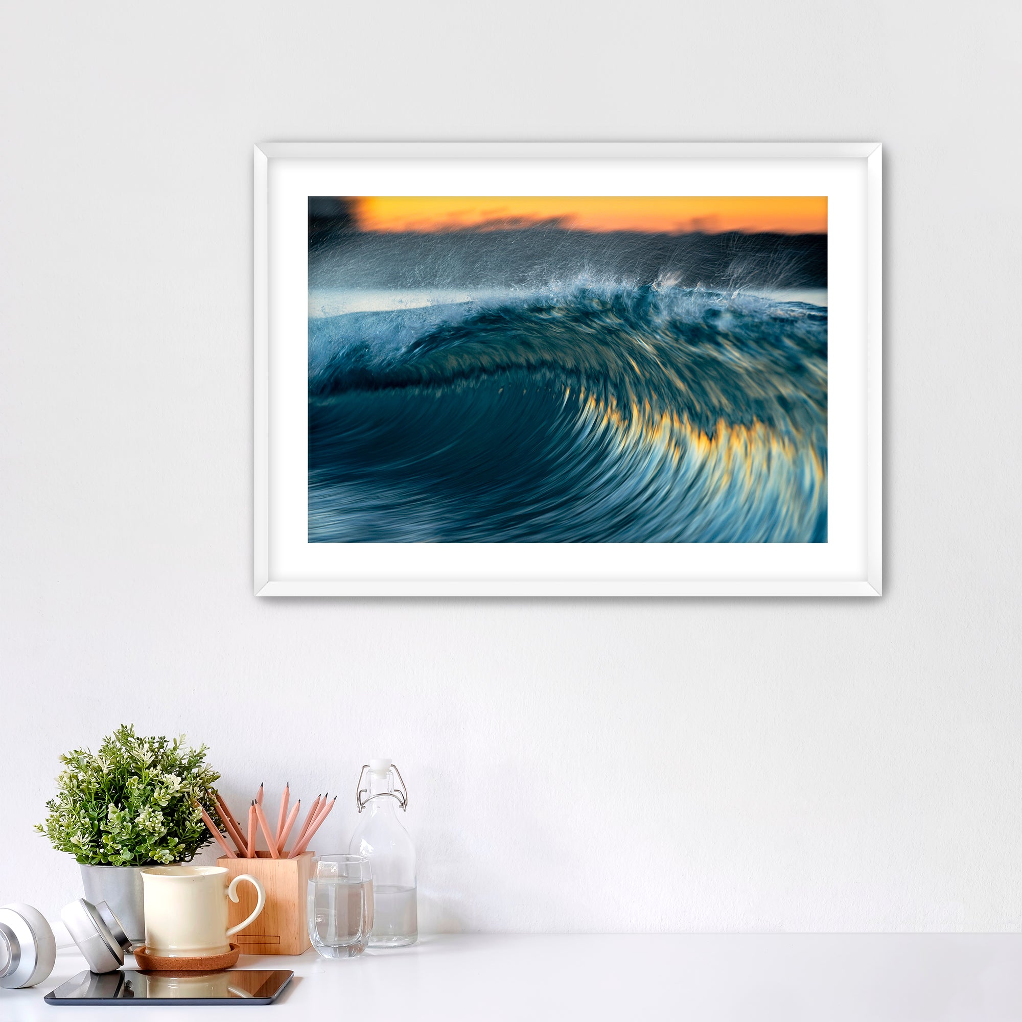 Framed photo of a colorful, slow-shutter wave on a wall above a desk with office supplies.