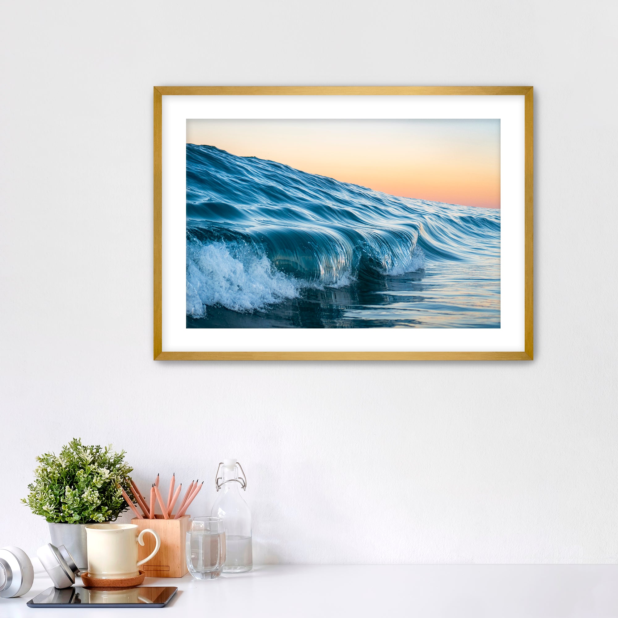 Framed photograph of a wave at Tamarack beach on a wall above a desk with office supplies.