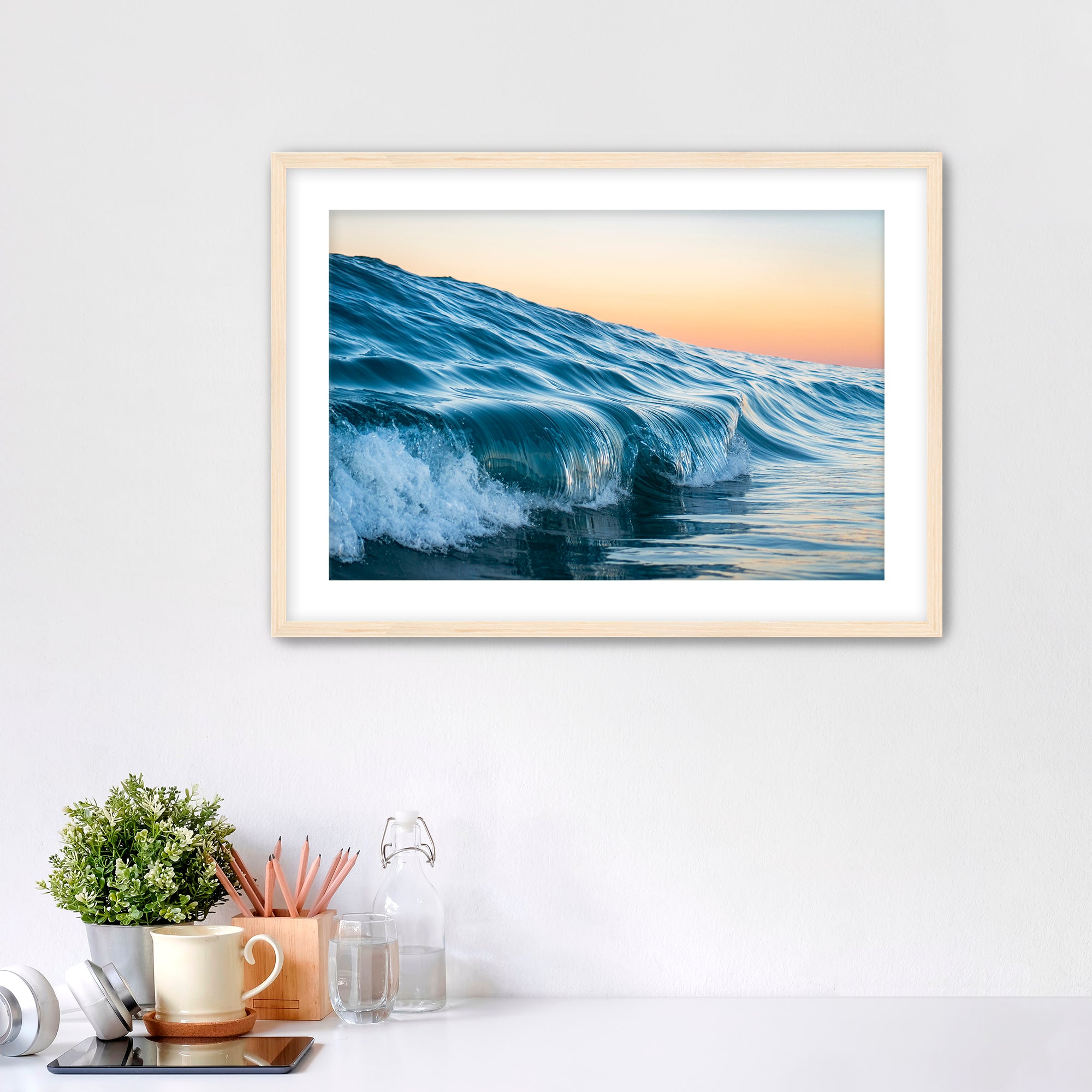 Framed photograph of a wave at Tamarack beach on a wall above a desk with office supplies.