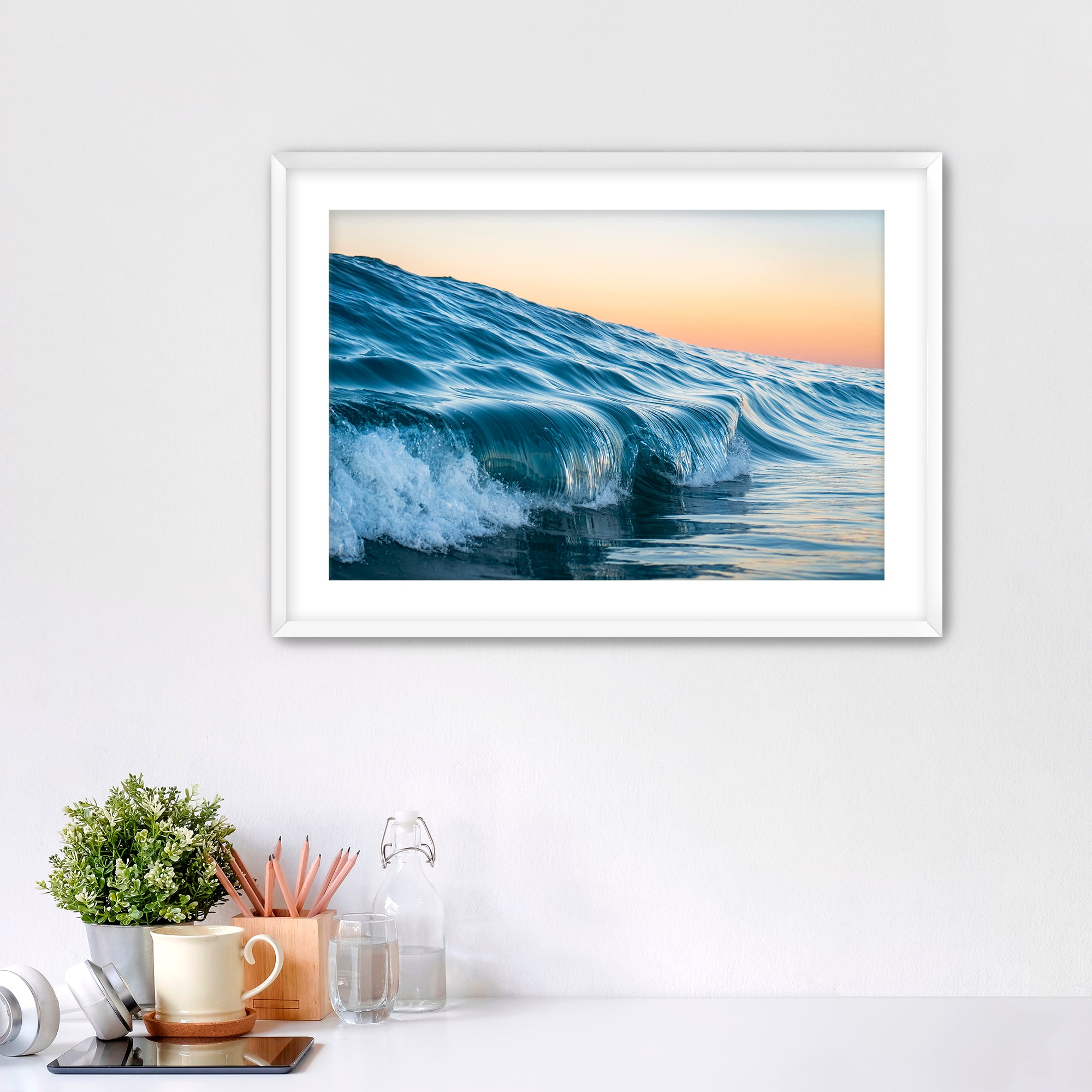 Framed photograph of a wave at Tamarack beach on a wall above a desk with office supplies.
