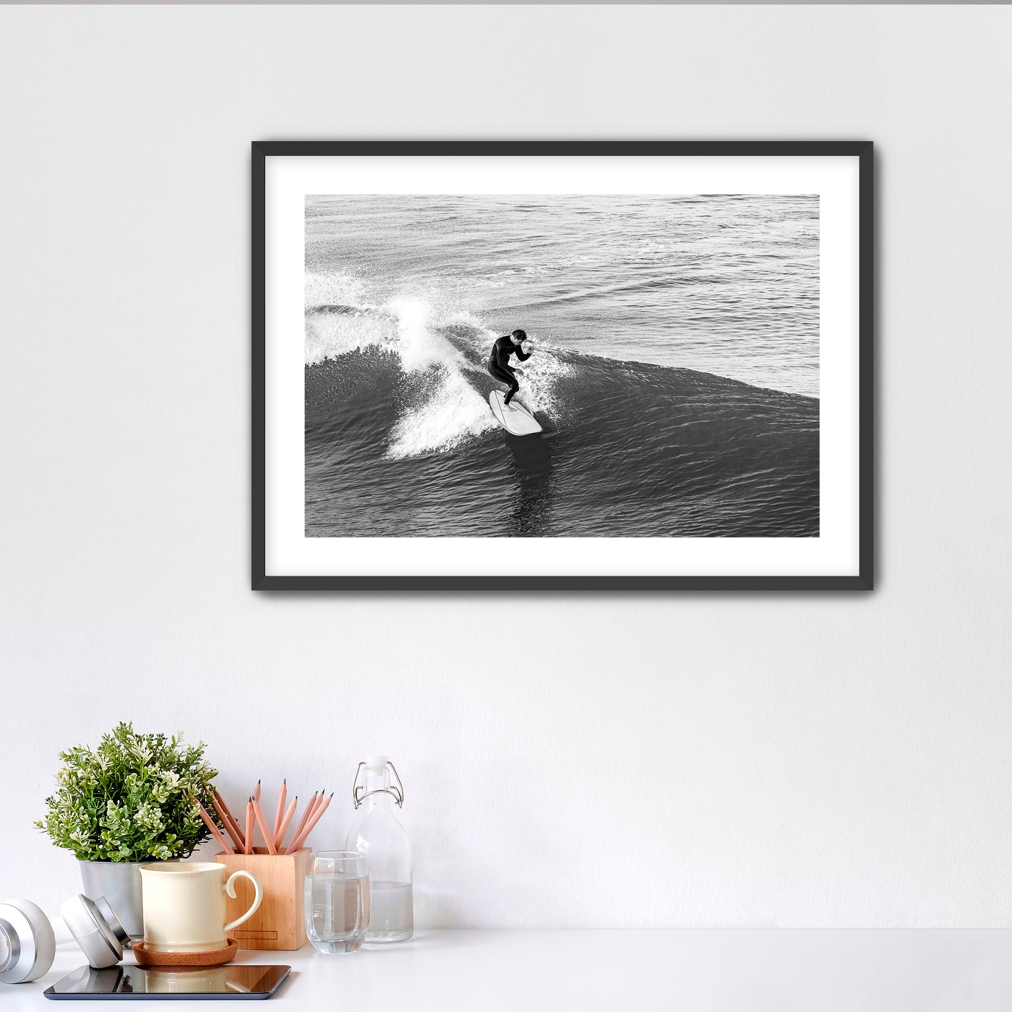 Framed black and white photograph of a surfer on a wave in a home office setting.