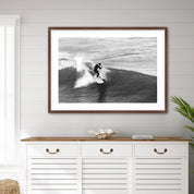 Framed black and white photograph of a surfer on a wave above a white cabinet with wooden top.