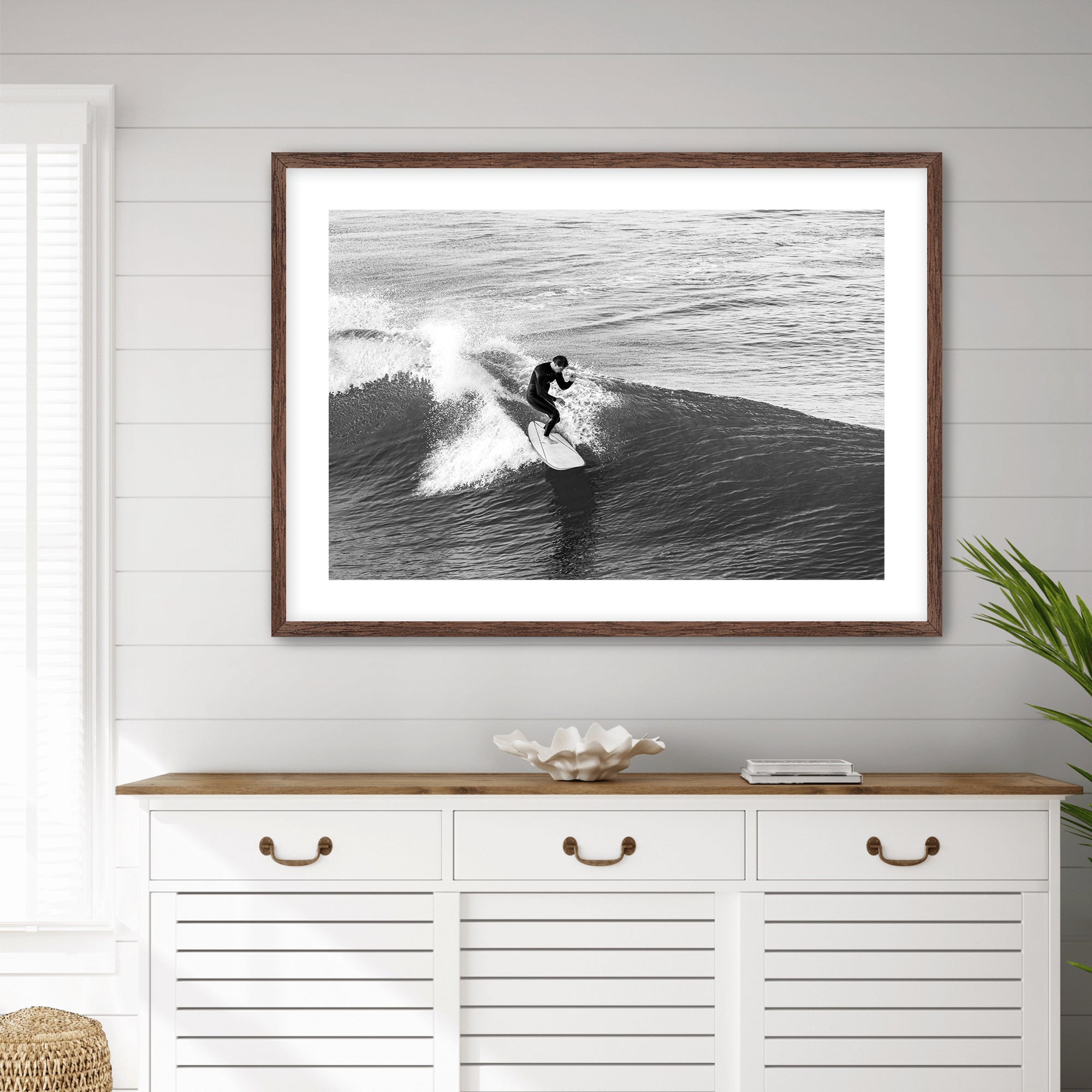 Framed black and white photograph of a surfer on a wave above a white cabinet with wooden top.