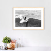 Framed black and white photograph of a surfer on a wave, displayed on a wall above a desk.