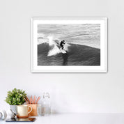 Framed black and white photograph of a surfer on a wave, displayed on a wall above a desk.