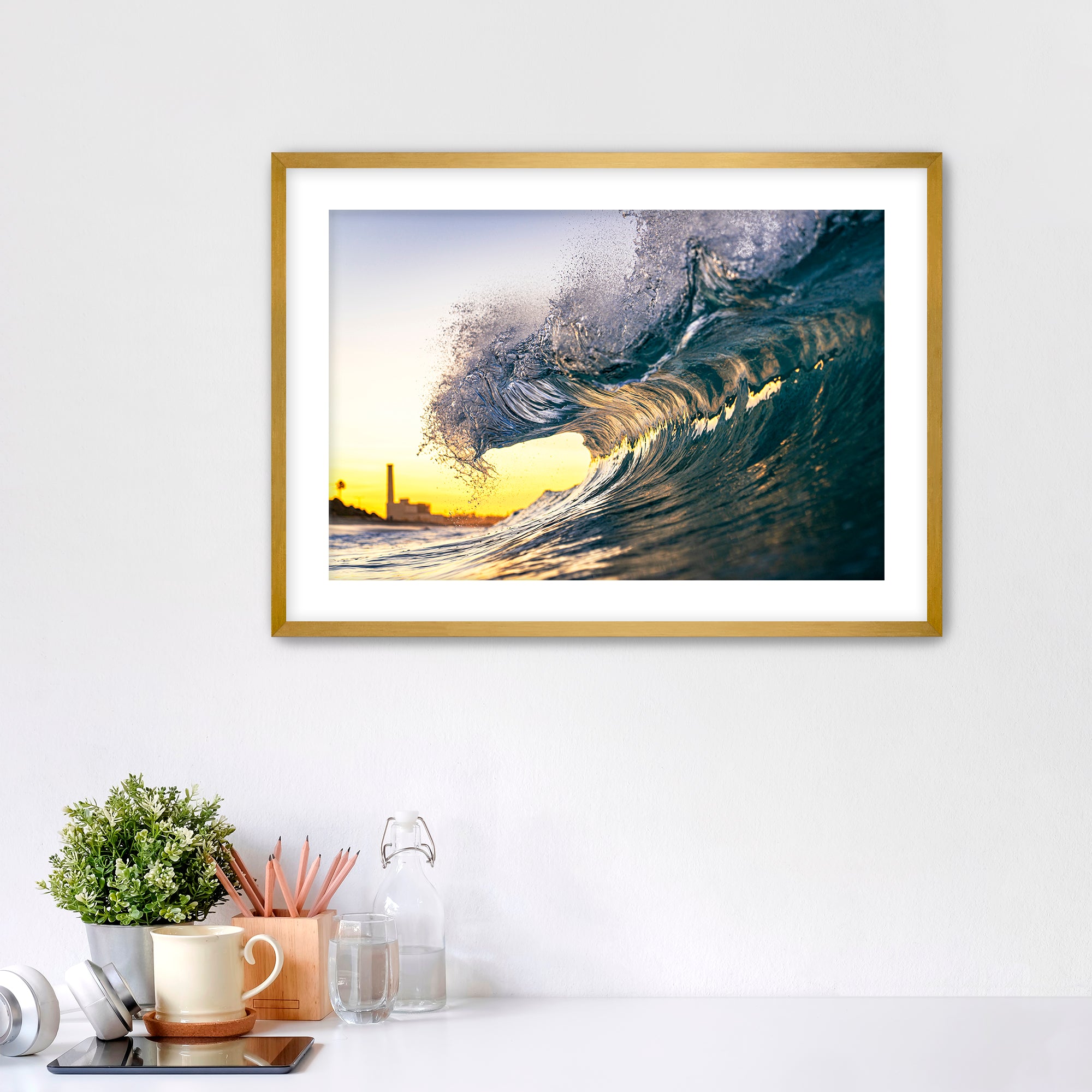Framed photograph of a wave at sunrise on a wall above a desk with office supplies.