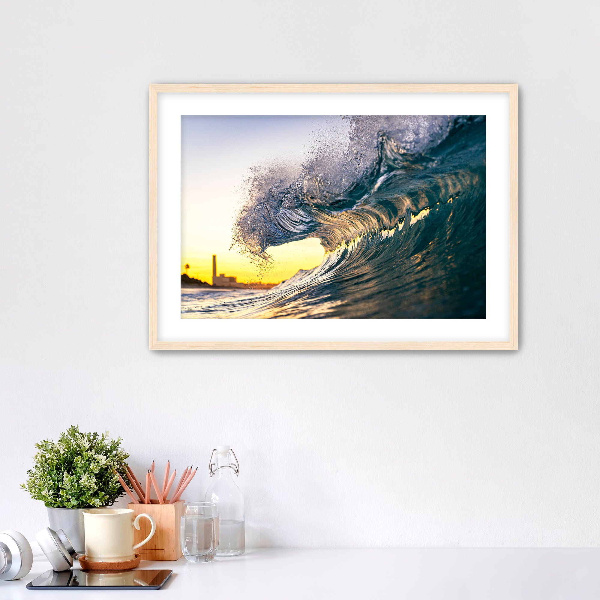 Framed photograph of a wave at sunrise on a wall above a desk with office supplies.