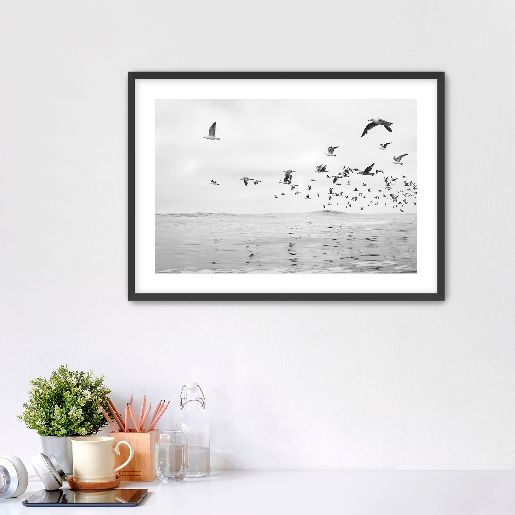 Framed artwork of birds flying over water on a white wall above a desk. Tamarack Beach, Carlsbad, California. 